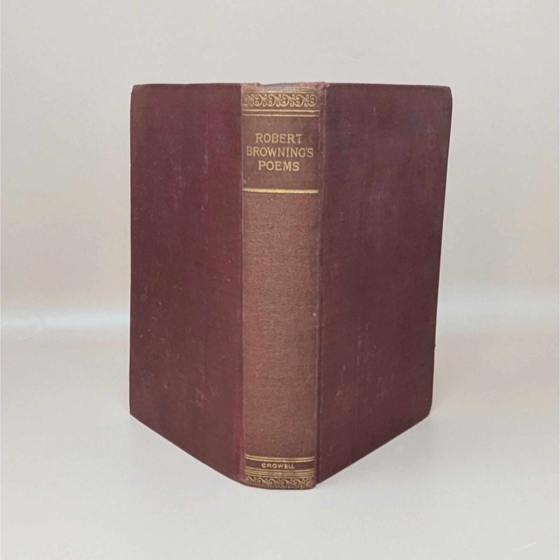 A burgundy cloth-bound hardcover book standing upright, featuring gilded typography on the spine for Robert Browning's Poems against a neutral background.