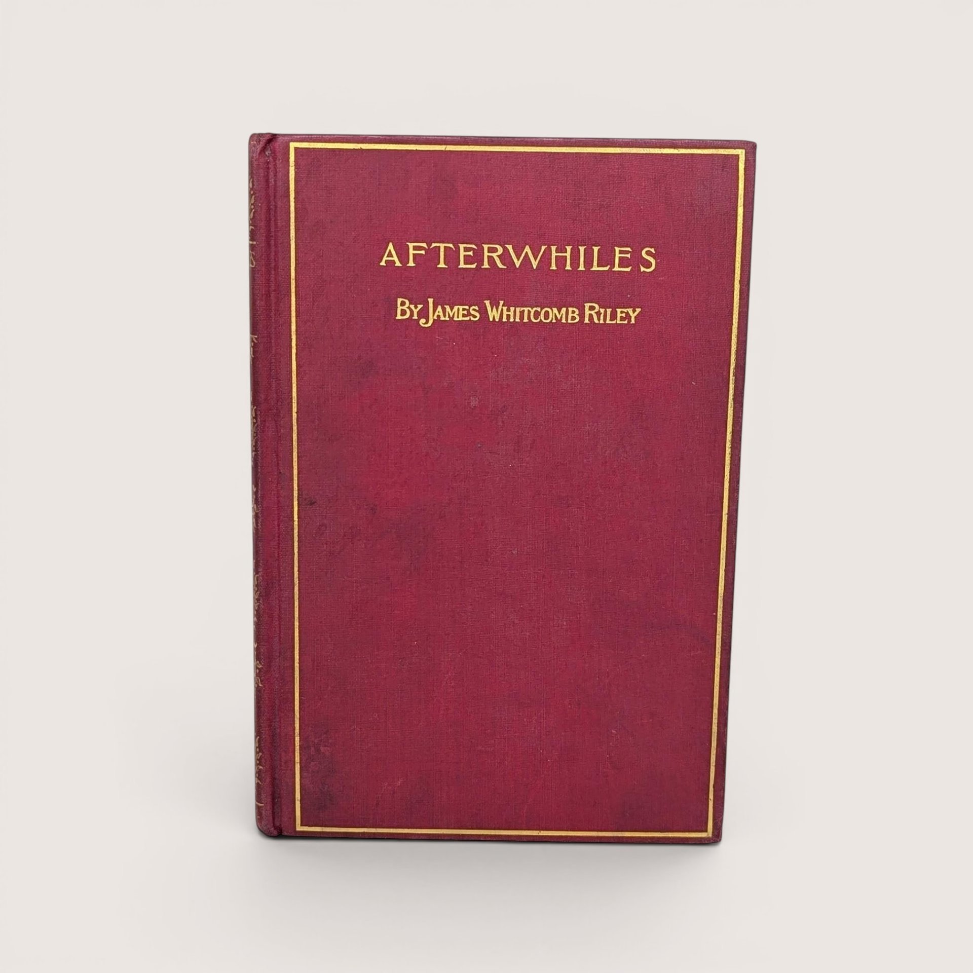 A burgundy cloth-bound hardcover book with a gilded rectangular border and gold typography for Afterwhiles by James Whitcomb Riley against a neutral background.