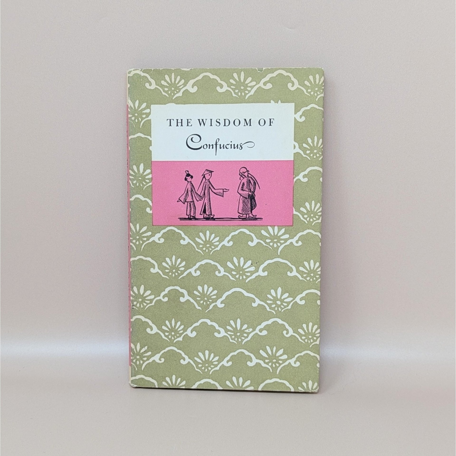 A slim hardcover book with a sage green and cream floral pattern, featuring a central pink and white label with the title The Wisdom of Confucius and a small illustration of three figures against a neutral background.