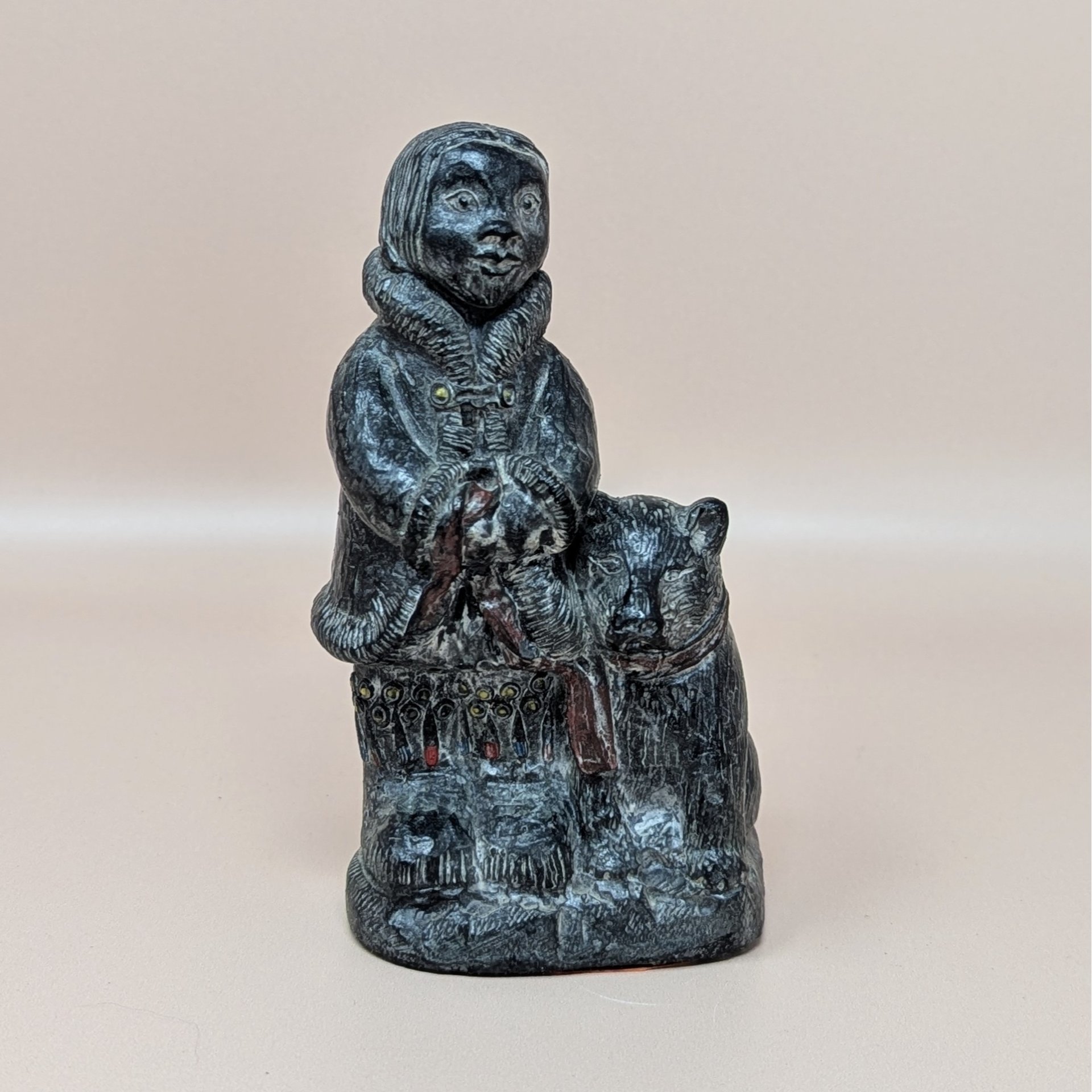 vintage black resin figurine depicting an Eskimo child in a fur-trimmed parka standing next to a large dog, featuring hand-painted red and blue details on the garment over a neutral tan background.
