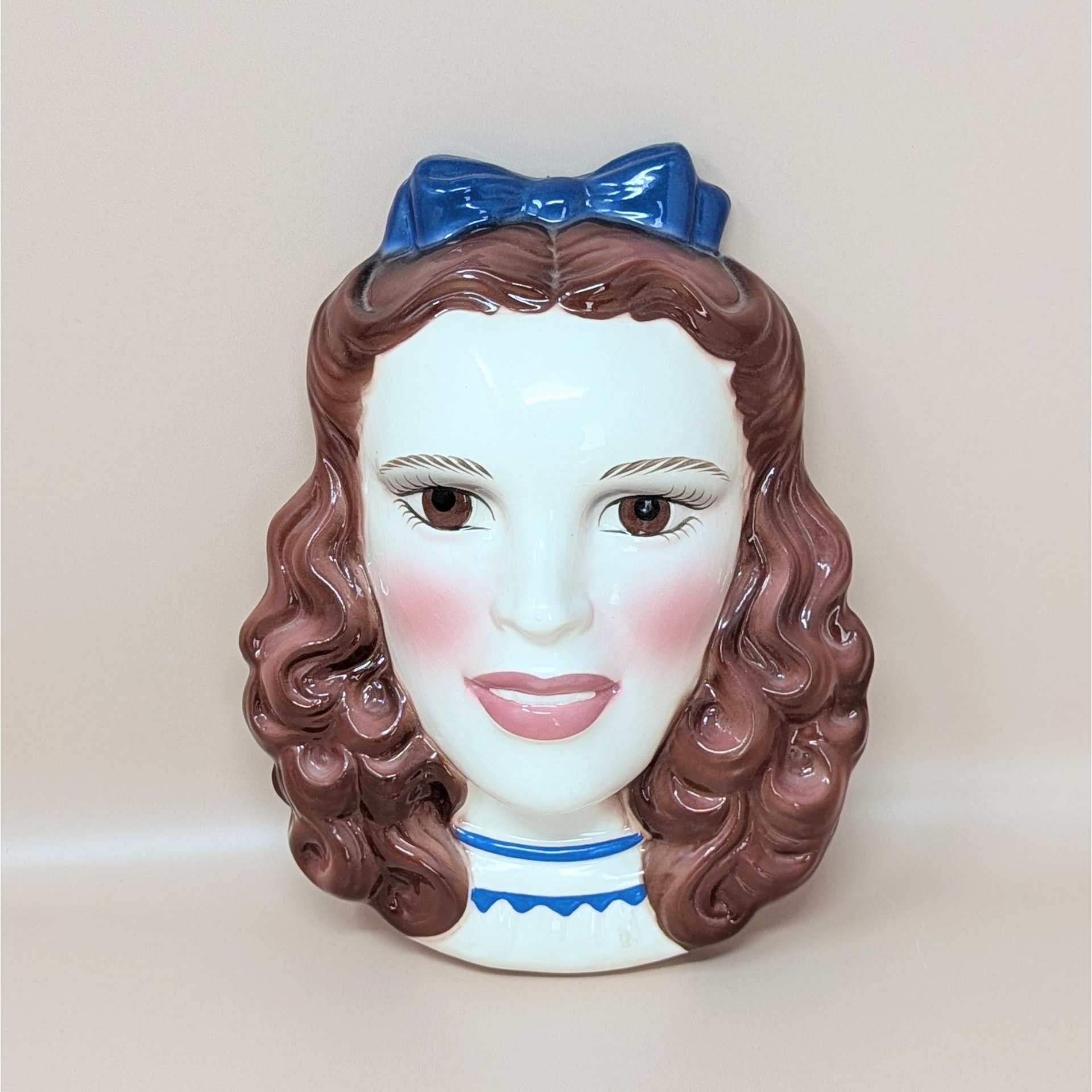 A vintage hand-painted ceramic wall mask of Dorothy from The Wizard of Oz, featuring her iconic pigtails and a bright blue hair bow.