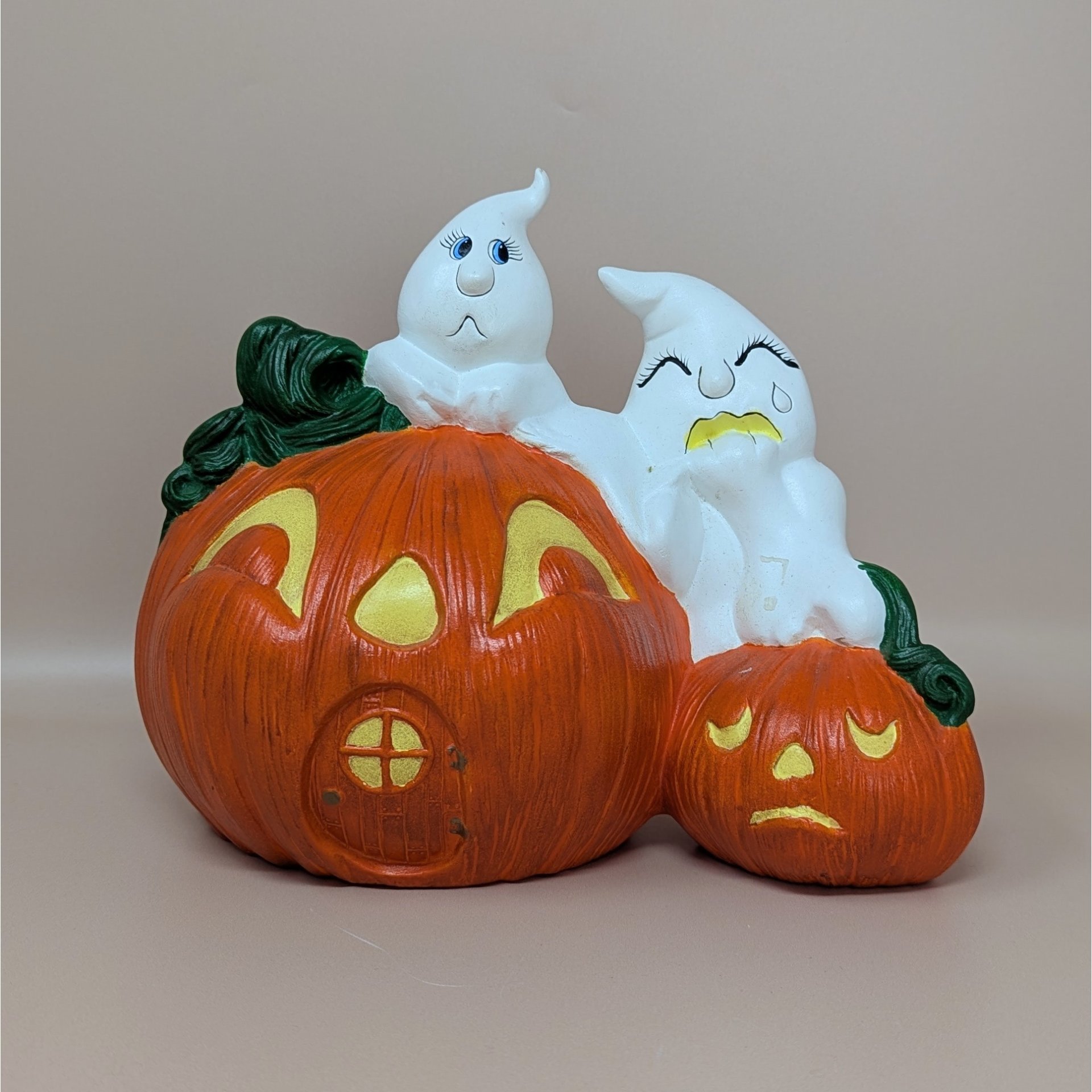 A vintage hand-painted ceramic figurine featuring two white ghosts perched atop a large orange jack o' lantern house and a smaller sad pumpkin.