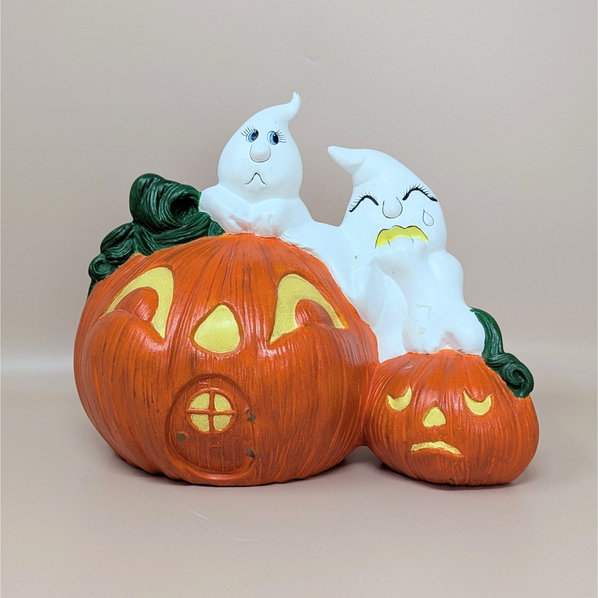 A vintage hand-painted ceramic figurine featuring two white ghosts perched atop a large orange jack o' lantern house and a smaller sad pumpkin.