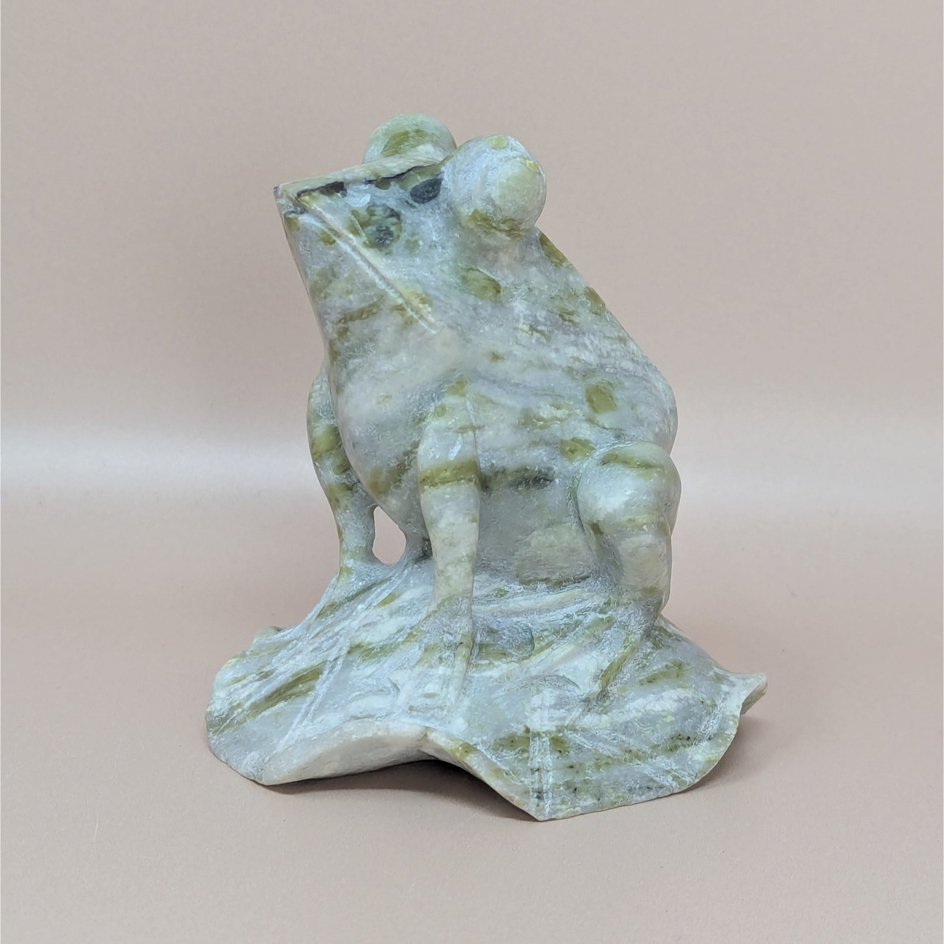 A vintage hand-carved nephrite jade figurine of a frog perched on a lily pad, showing natural pale green and olive marbling throughout the stone.