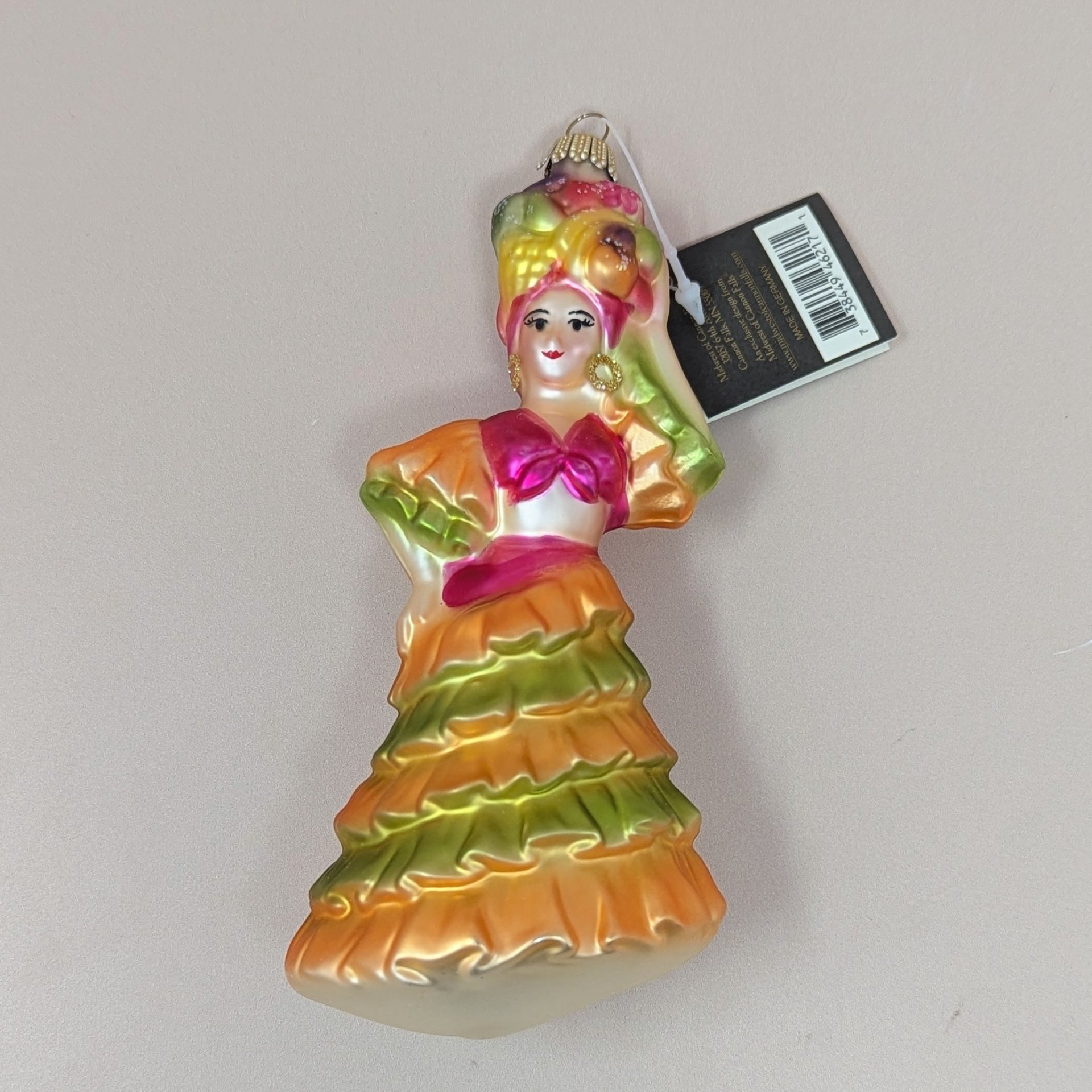 A vibrant vintage blown glass ornament of a dancer in a ruffled orange and lime green dress with a fruit basket headdress, still featuring its original Midwest tag.