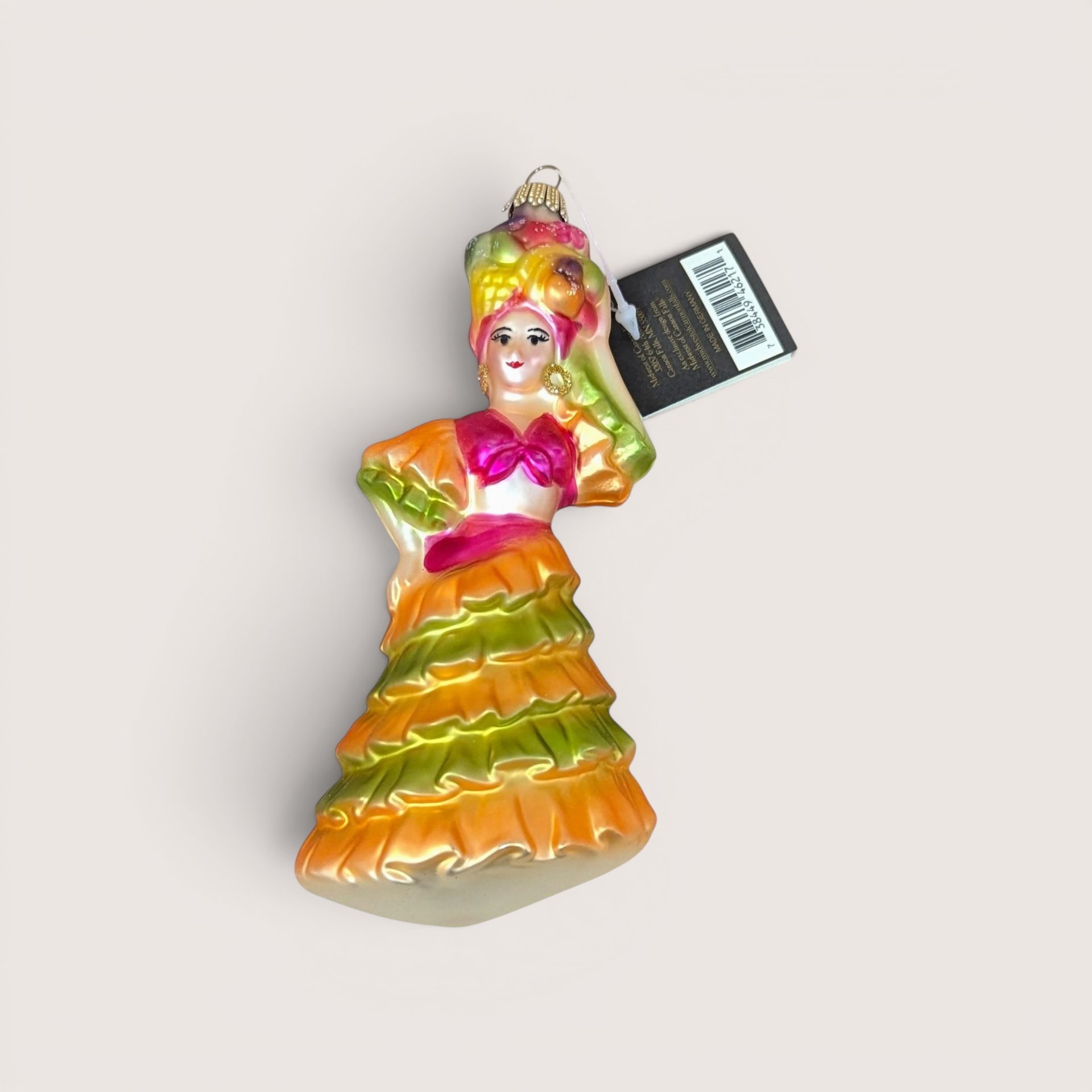 A vibrant vintage blown glass ornament of a dancer in a ruffled orange and lime green dress with a fruit basket headdress, still featuring its original Midwest tag.