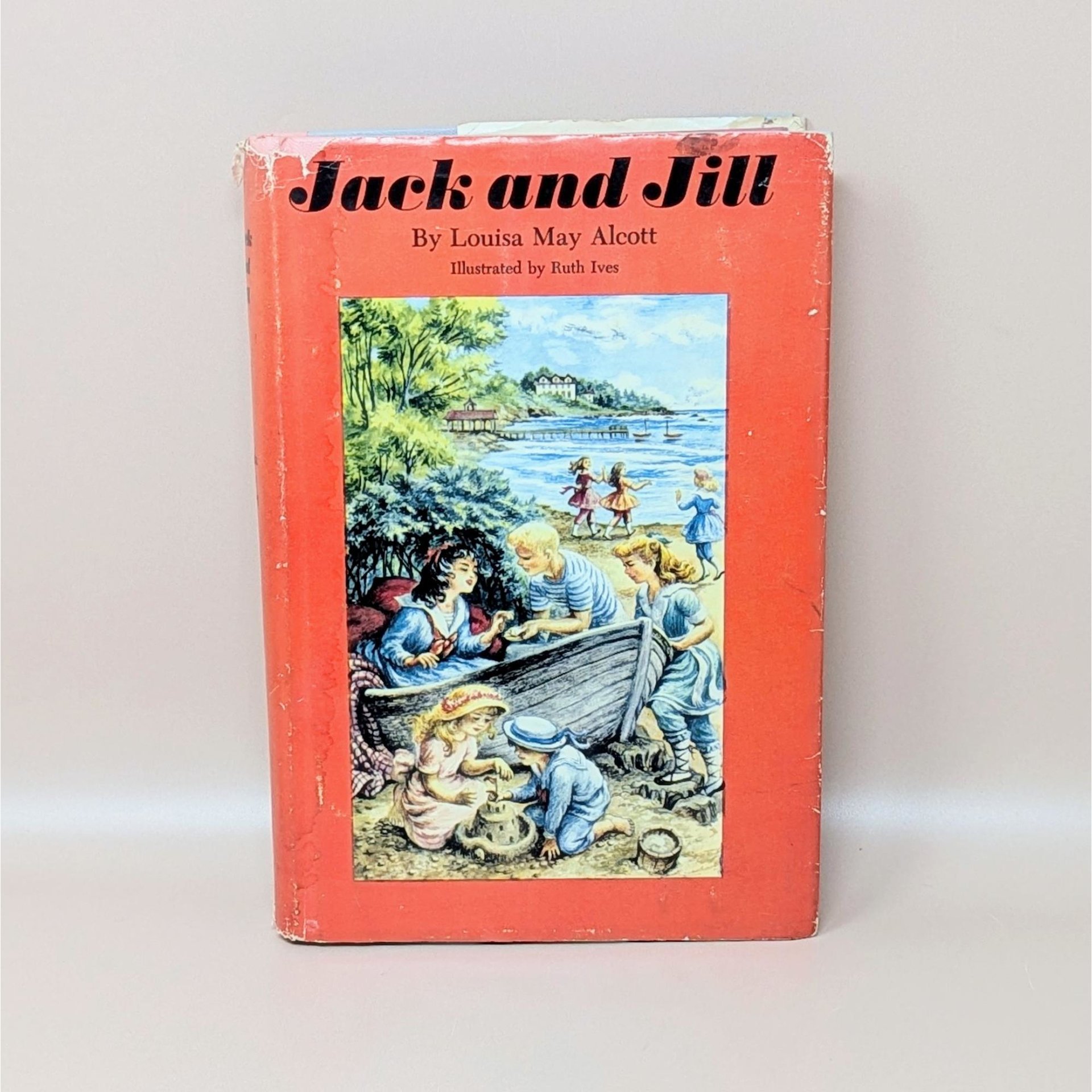 A vintage 1956 hardcover edition of Jack and Jill by Louisa May Alcott with a bright red dust jacket featuring children playing at the beach