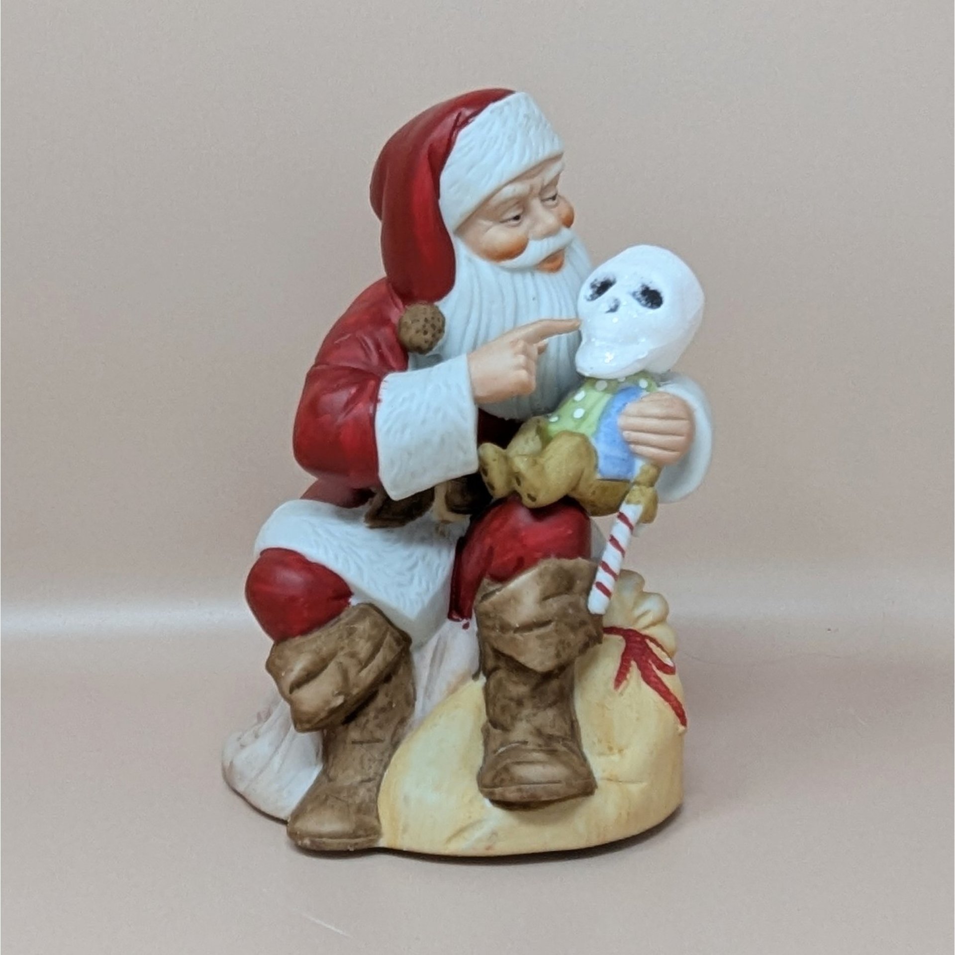 A modified vintage ceramic music box where Santa Claus holds a small figure that has been fitted with a custom styrofoam skull head.
