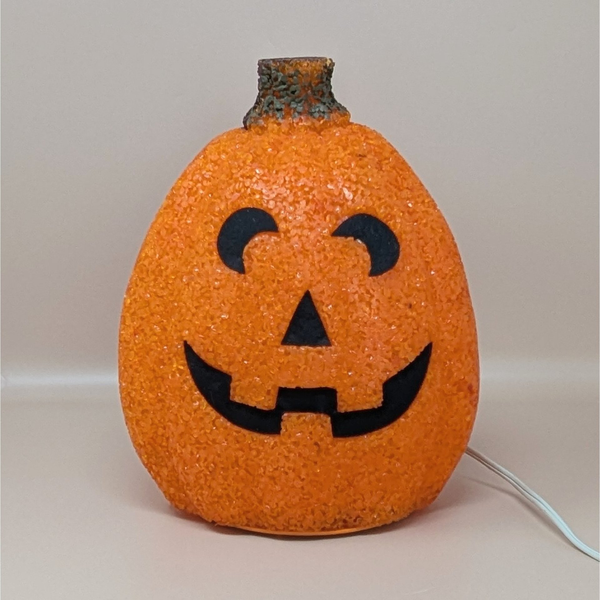 A vintage orange melted plastic "popcorn" Jack O'Lantern light with a smiling black face and a green stem on top.
