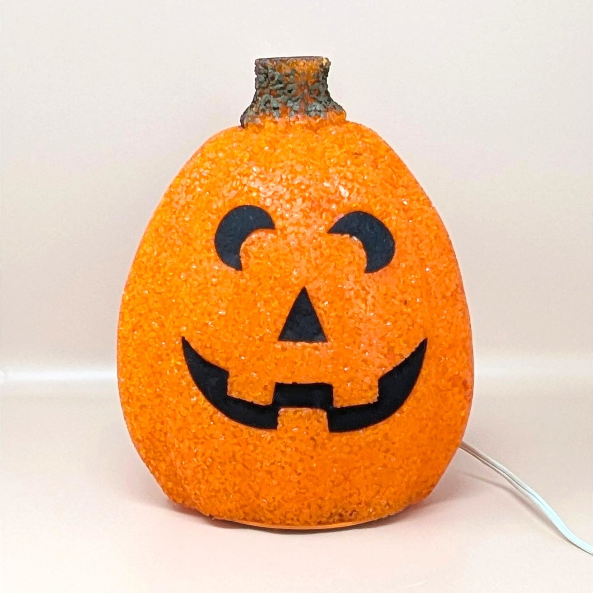 A vintage orange melted plastic "popcorn" Jack O'Lantern light with a smiling black face and a green stem on top.