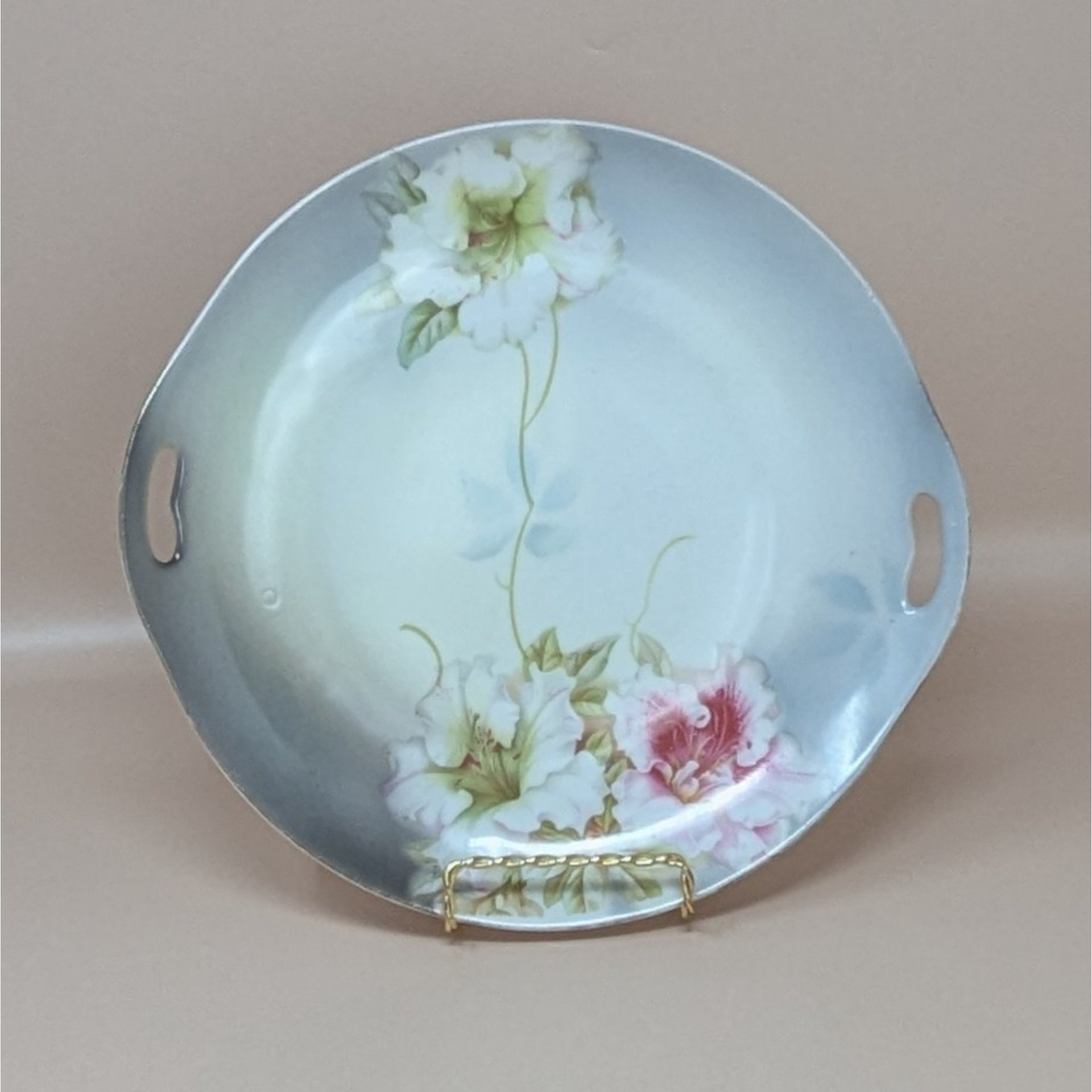 A vintage round porcelain dresser tray from PV Vessra Germany, featuring hand-painted white and pink lilies against a soft grey and cream background with gold trim.