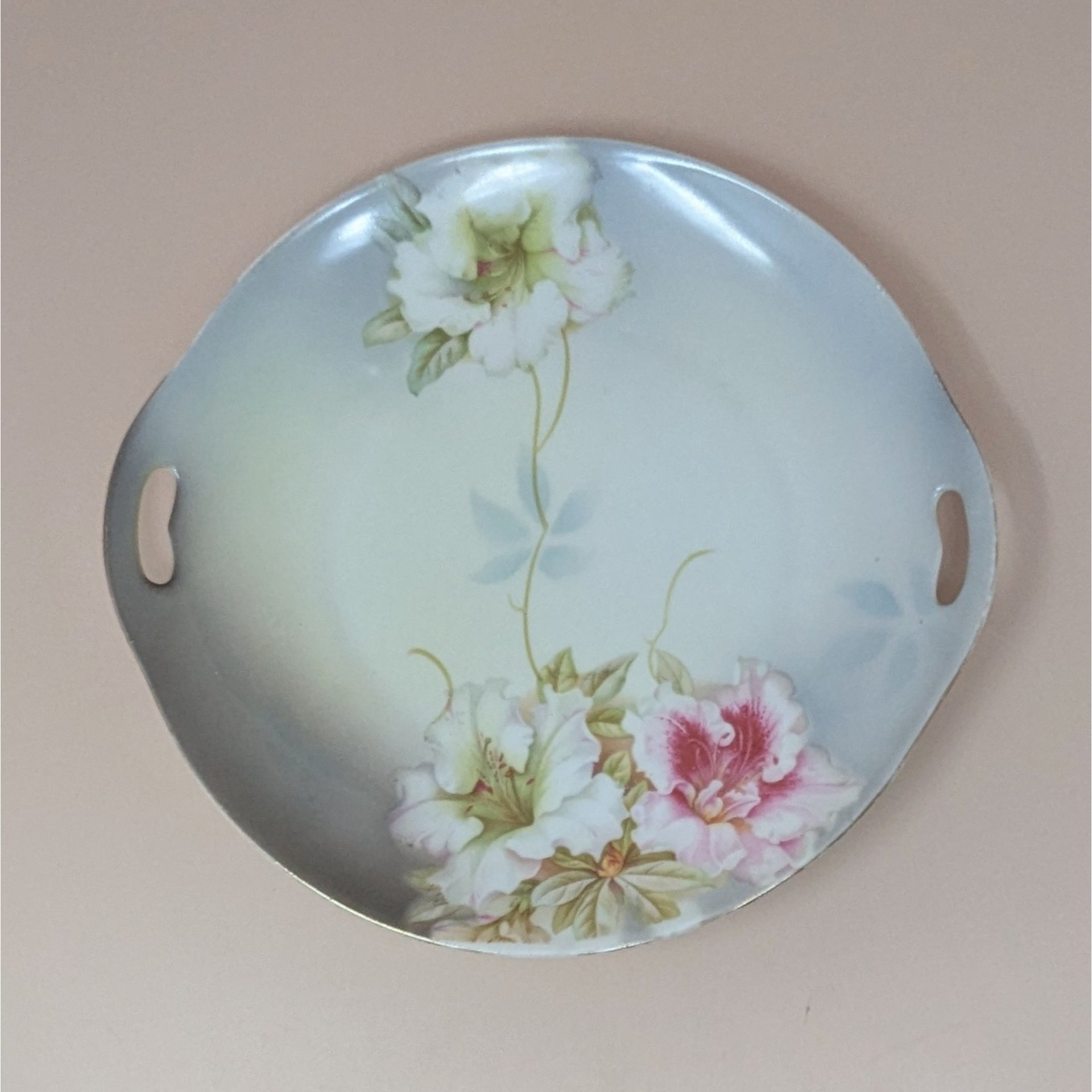 A vintage round porcelain dresser tray from PV Vessra Germany, featuring hand-painted white and pink lilies against a soft grey and cream background with gold trim.