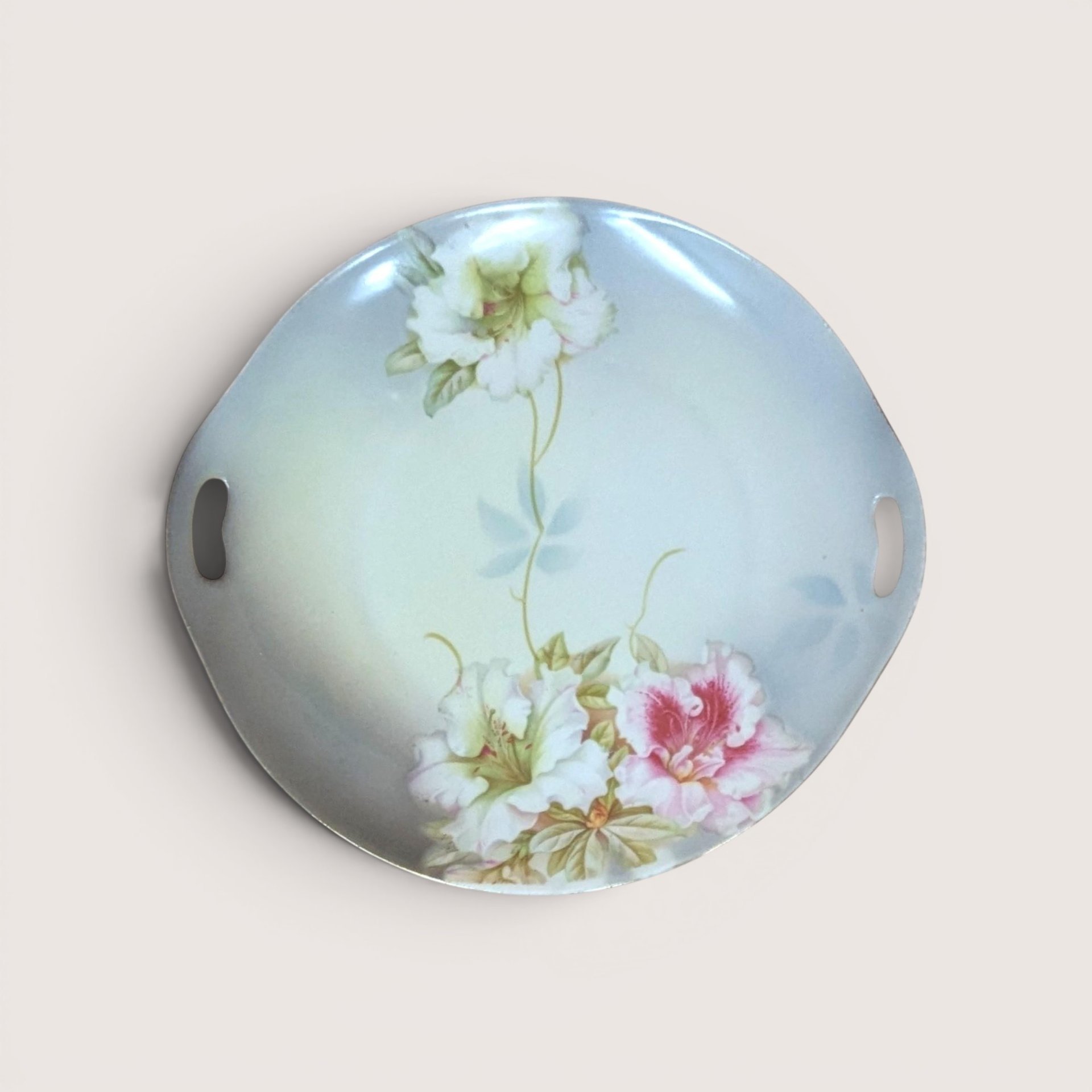 A round porcelain handled plate with painted pink and white floral details, centered on a beige background.