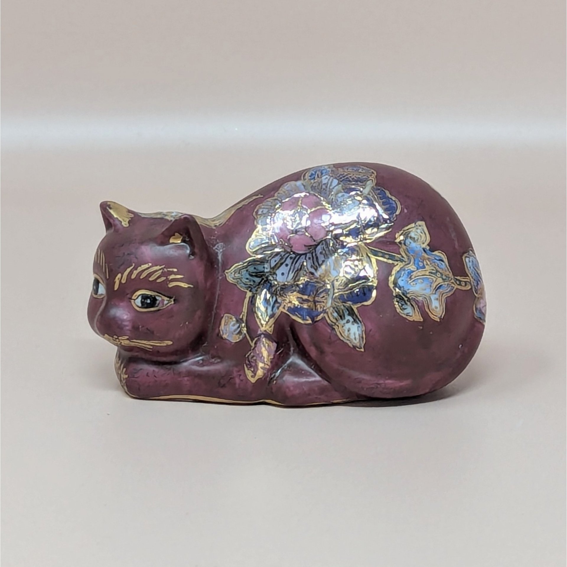 A vintage FF Fine Florals ceramic cat figurine in a matte plum finish with hand-painted blue flowers and a gold "Made in China" sticker on the base.