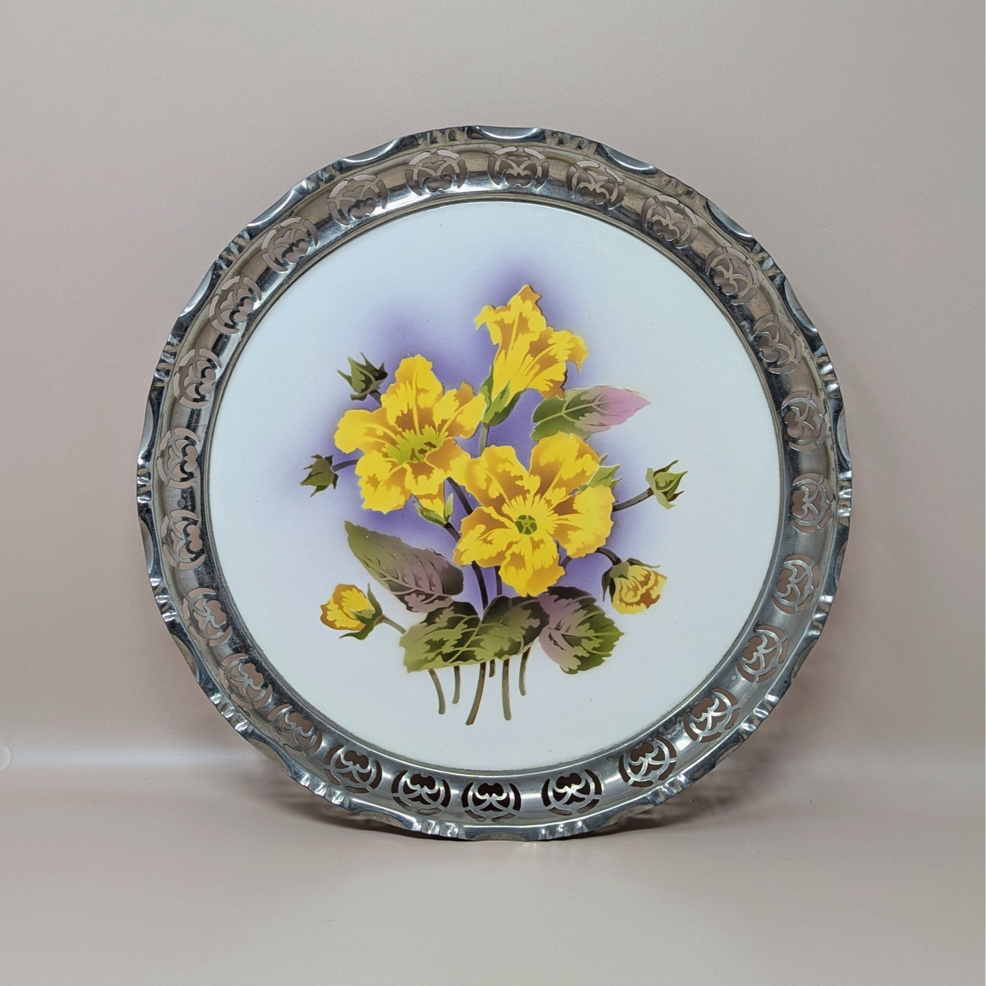 A vintage round porcelain tray featuring bright yellow flowers with a purple shadow background, enclosed in a decorative pierced silver metal rim