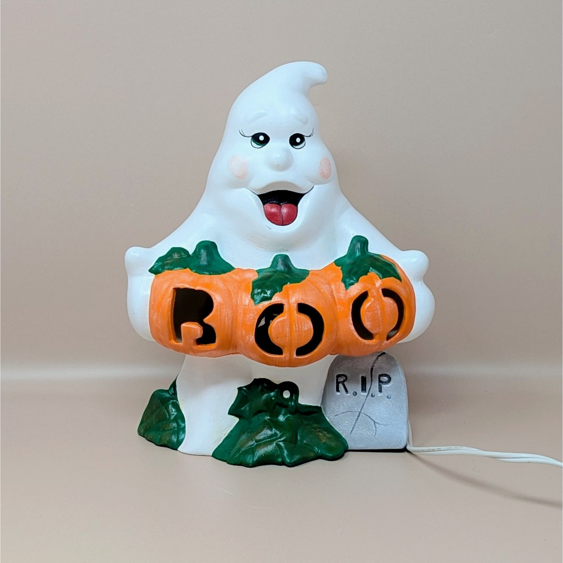 A hand painted vintage white ceramic ghost in file C2059 1.jpg holding three orange pumpkins that spell out BOO with a small grey RIP tombstone at the base
