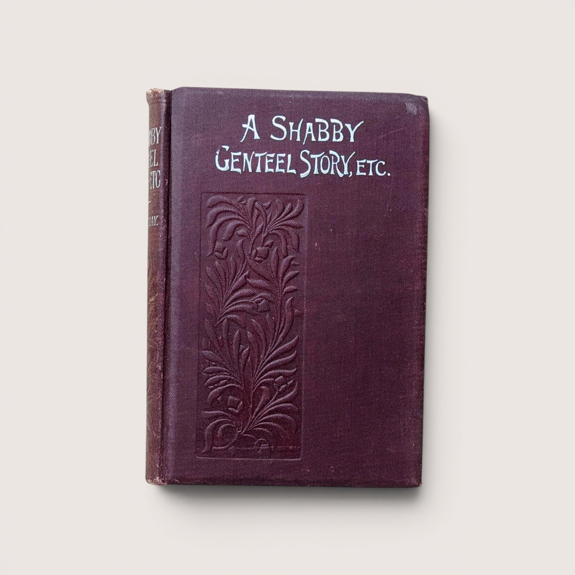 An antique burgundy book titled "A Shabby Genteel Story, Etc." with an embossed floral pattern on a beige background.
