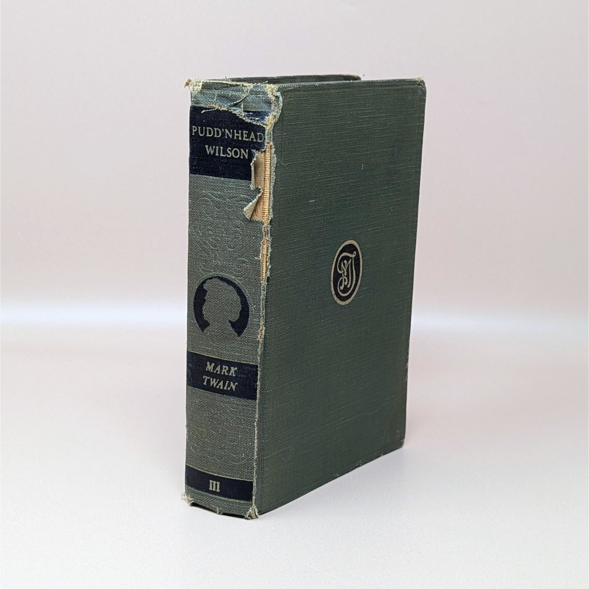Am anitque 1922 hardcover of Pudd'nhead Wilson by Mark Twain with a green cloth cover and a damaged spine showing the binding underneath