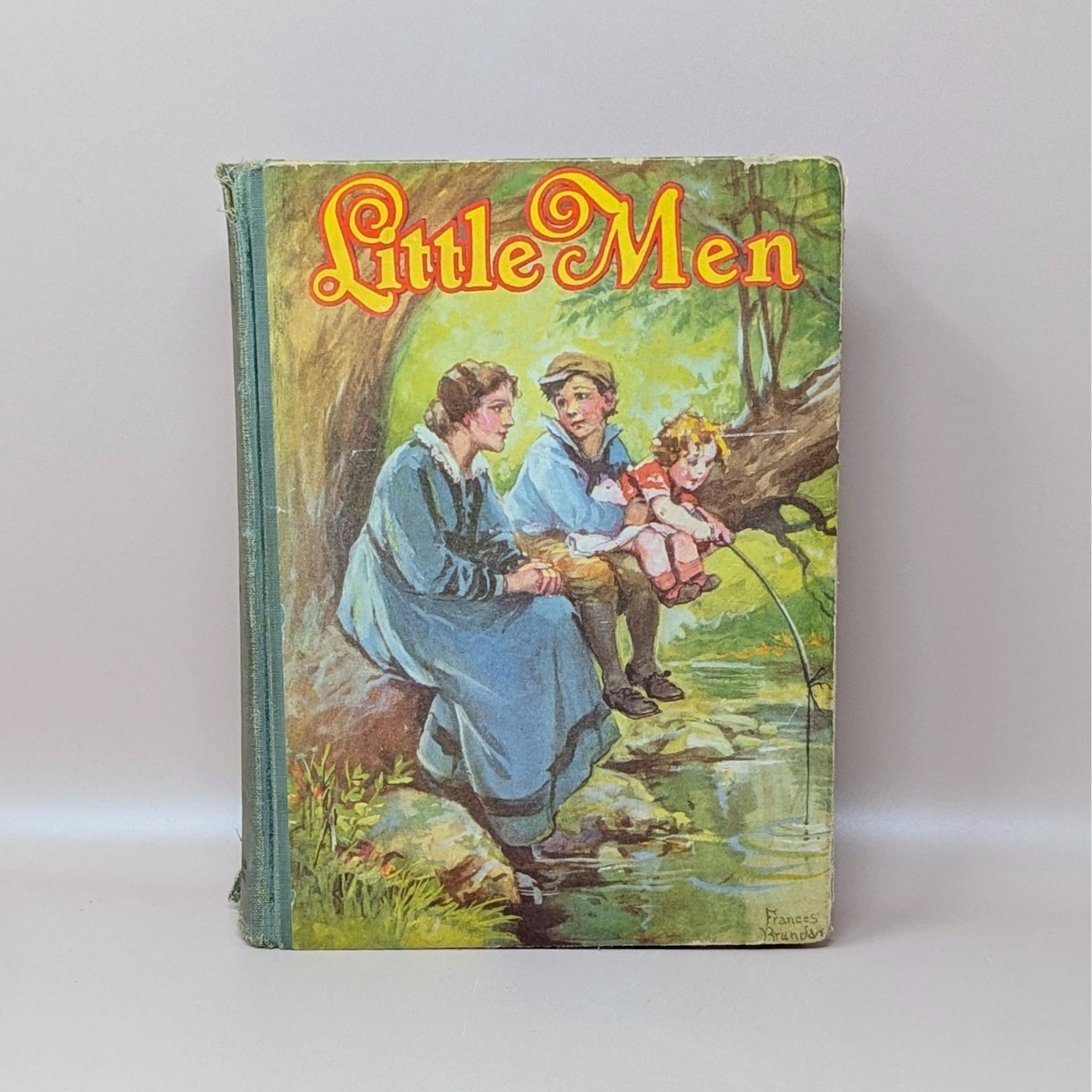 A vintage 1928 hardcover book titled Little Men by Louisa M. Alcott featuring a color illustration by Frances Brundage of children fishing by a stream