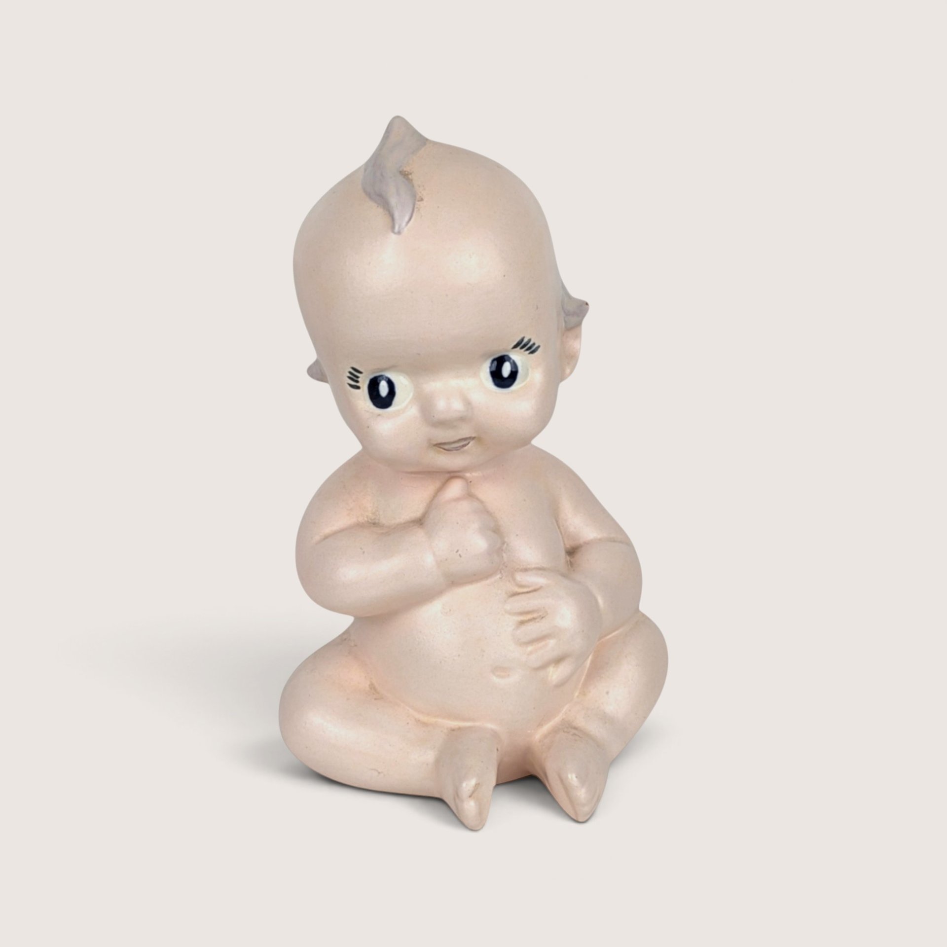 Vintage ceramic baby doll powder shaker in a seated pose with a topknot and painted facial features.