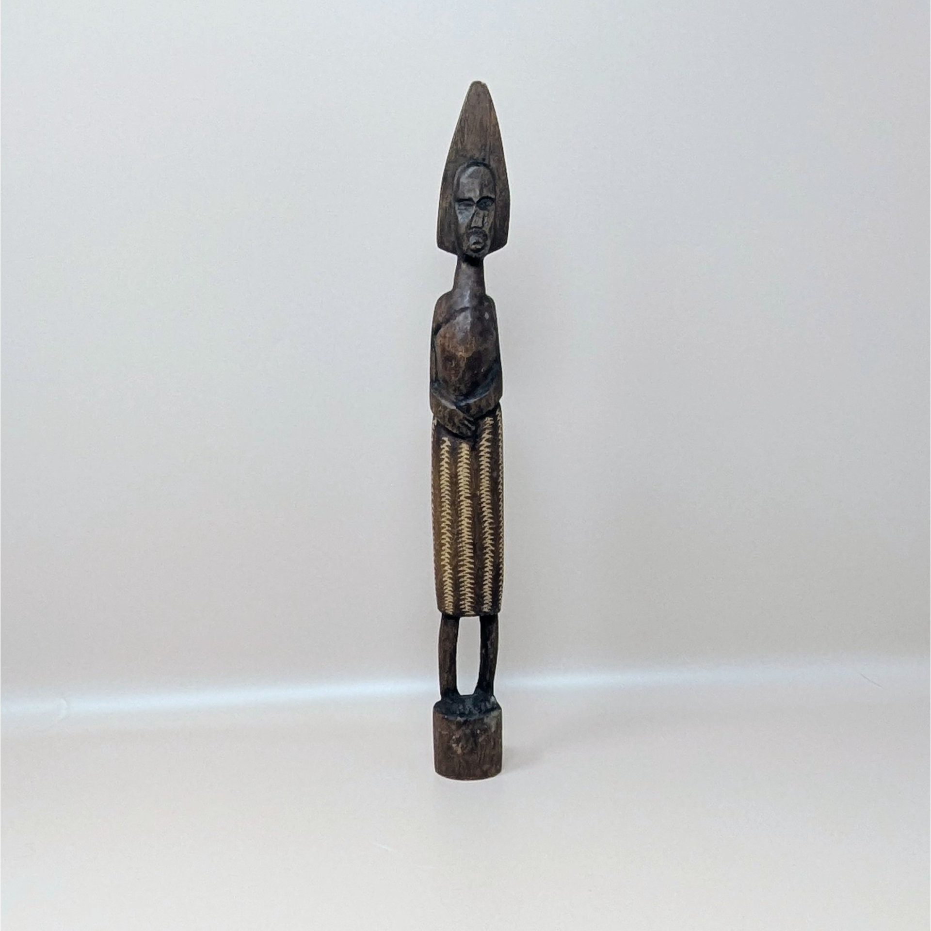 A vintage slender hand carved dark wood African figurine with a tall pointed headdress and a textured patterned skirt