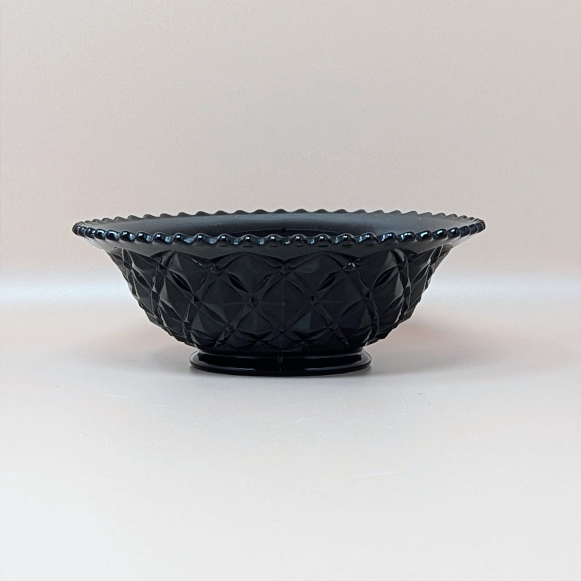 A vintage footed bowl in ebony black glass featuring a deep diamond block pressed pattern and a scalloped rim