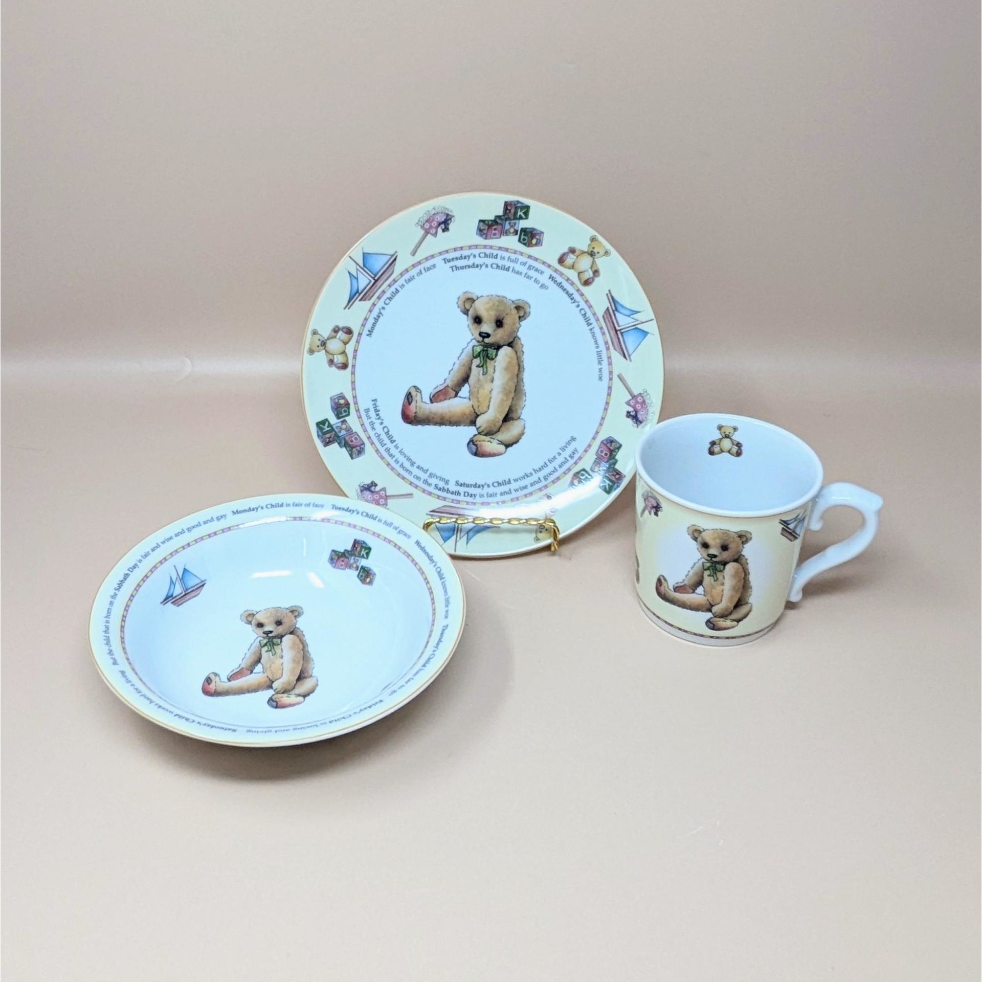 A three piece Royal Worcester porcelain nursery set including a plate, bowl, and mug featuring a teddy bear and the Monday's Child poem