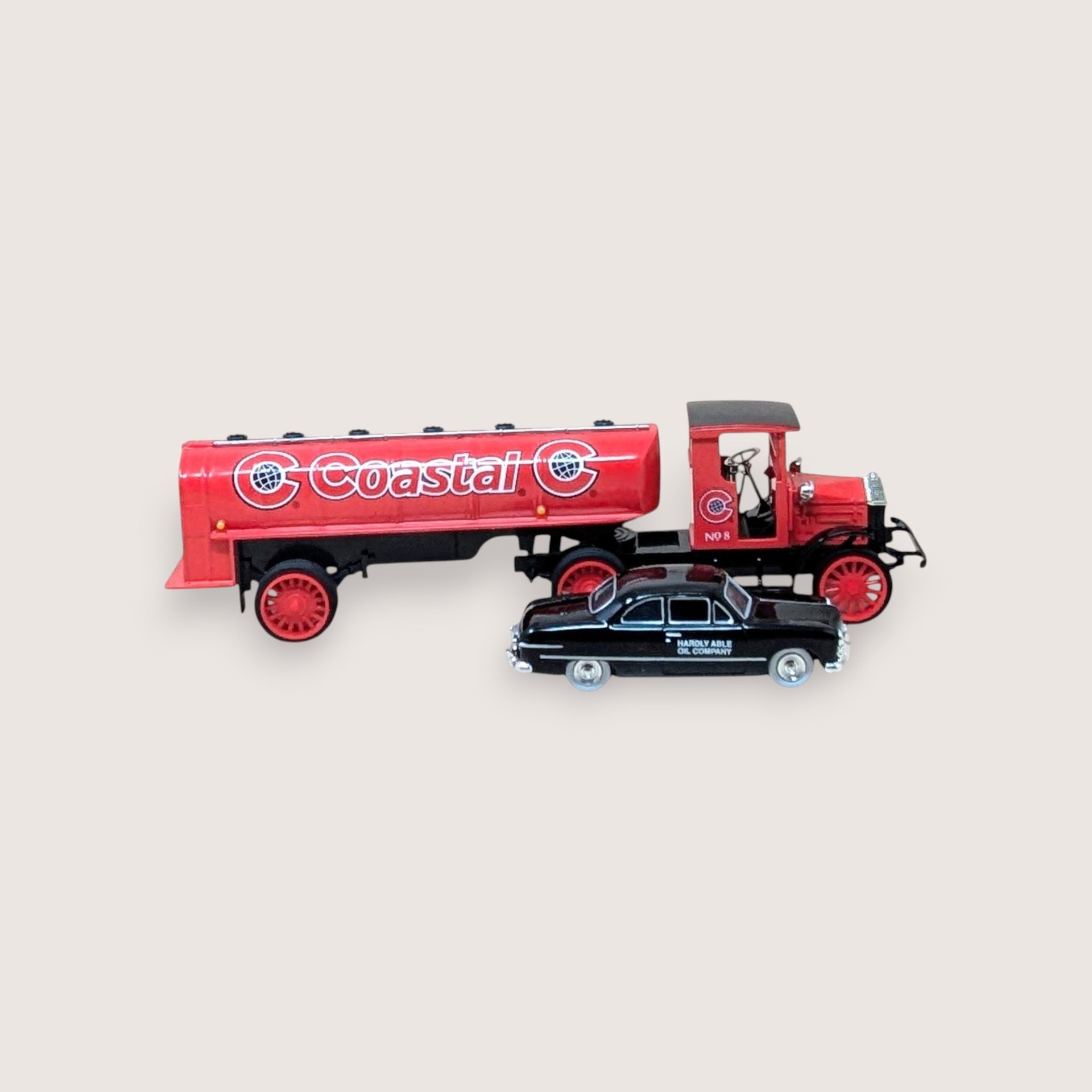 A vintage miniature red Coastal oil tanker truck alongside a small black car on a plain light background.