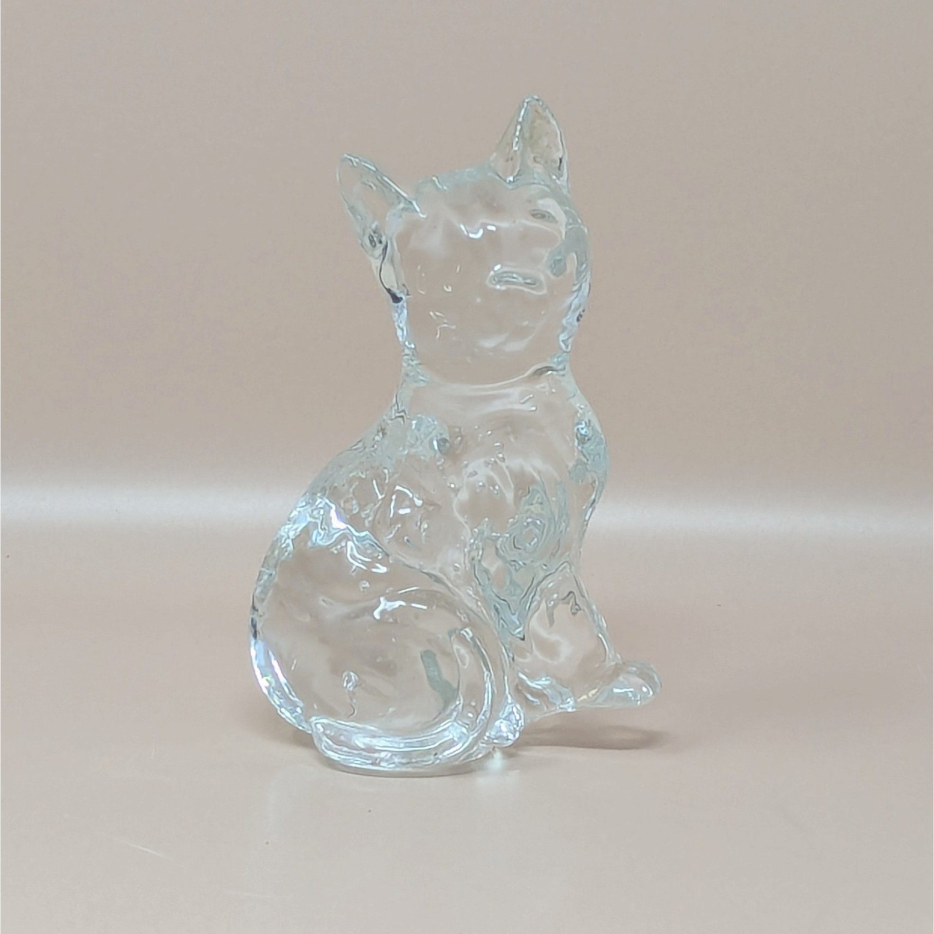 A vintage solid clear glass figurine of a sitting cat with pointed ears and a curled tail