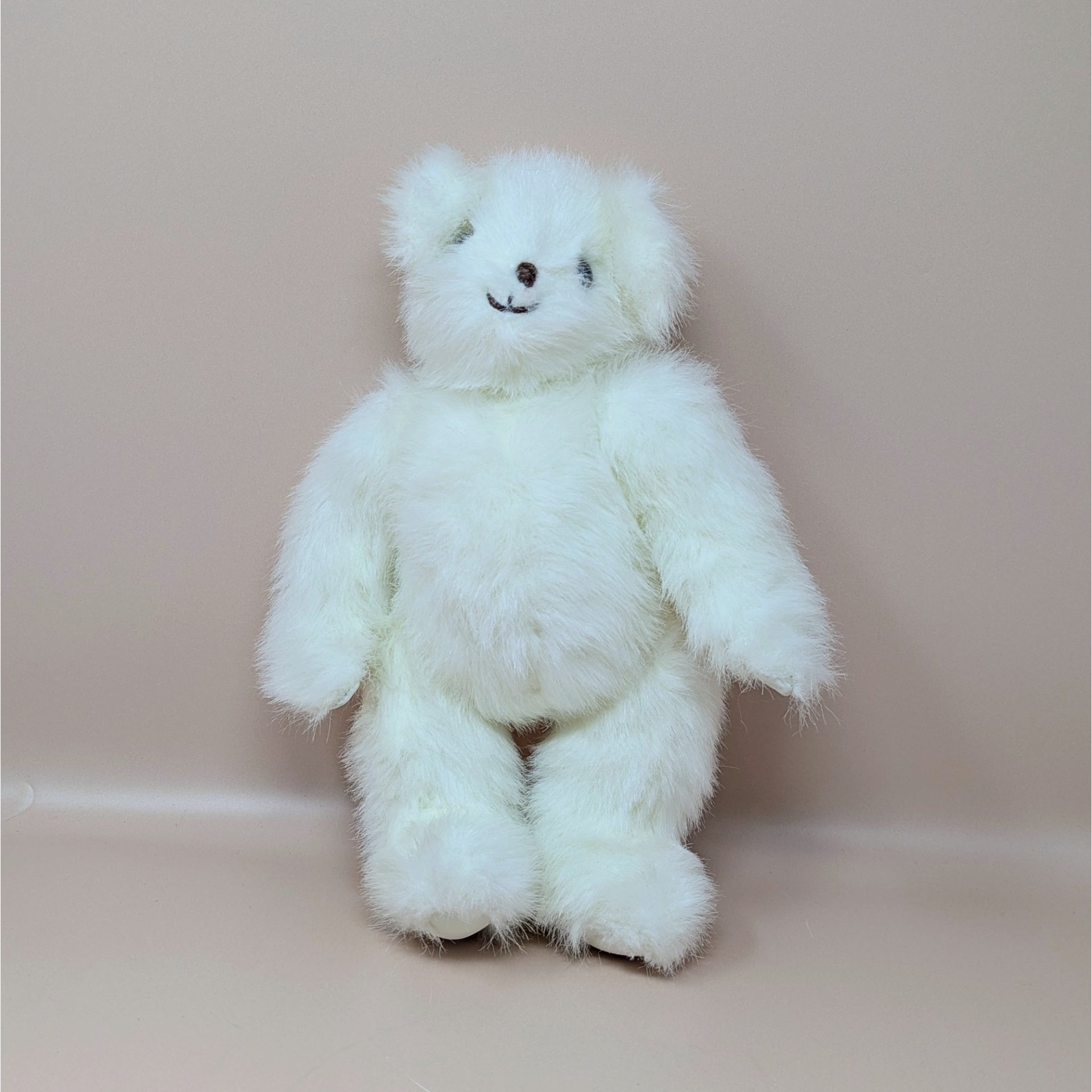 A vintage white jointed teddy bear by artist Joan Chesney with fluffy fur and a hand stitched smile