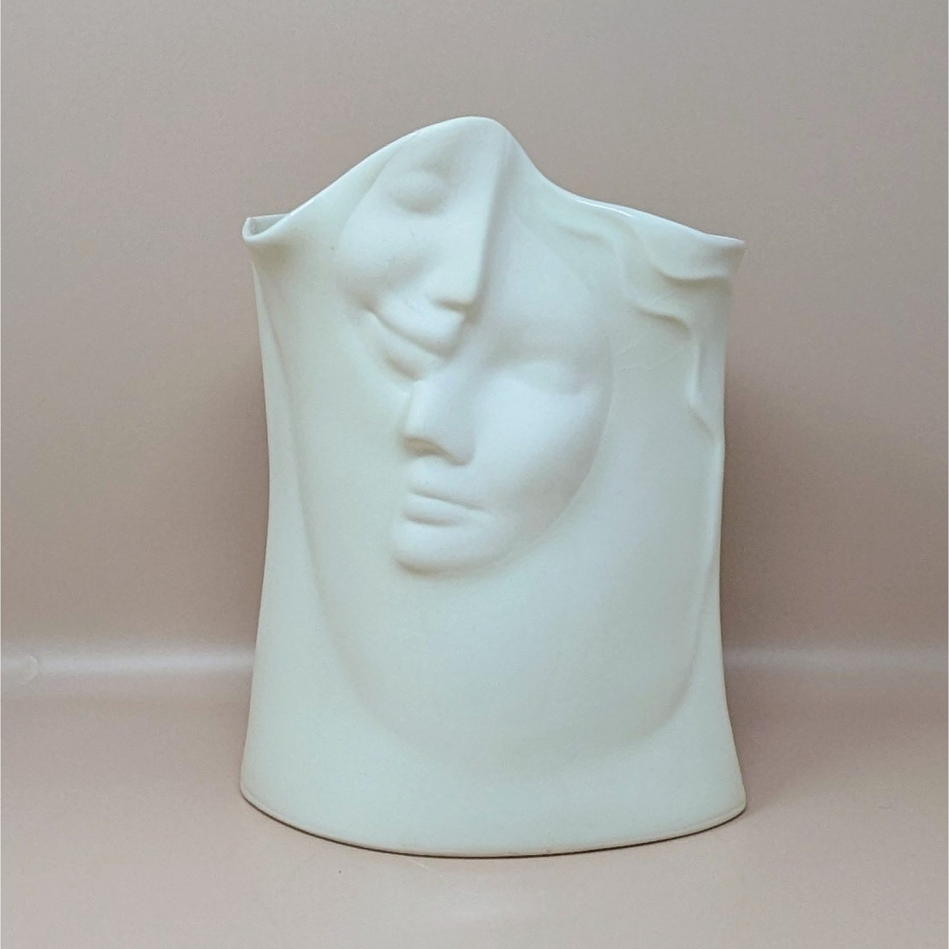 Front view of a white porcelain vase featuring two serene faces in relief. The faces overlap with soft, flowing lines against a neutral background.