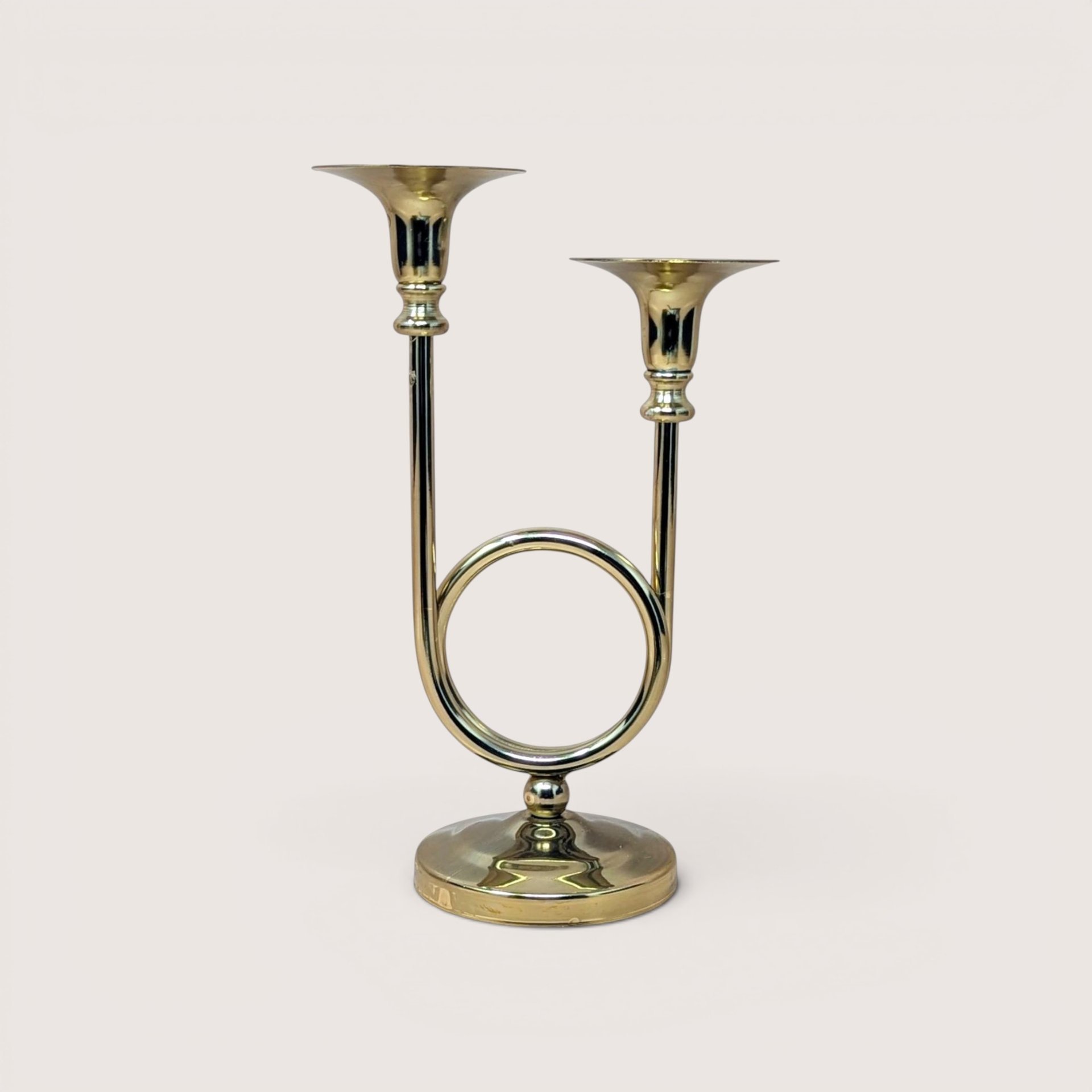 A polished gold-tone brass double taper candle holder shaped like a French horn on a round pedestal base.