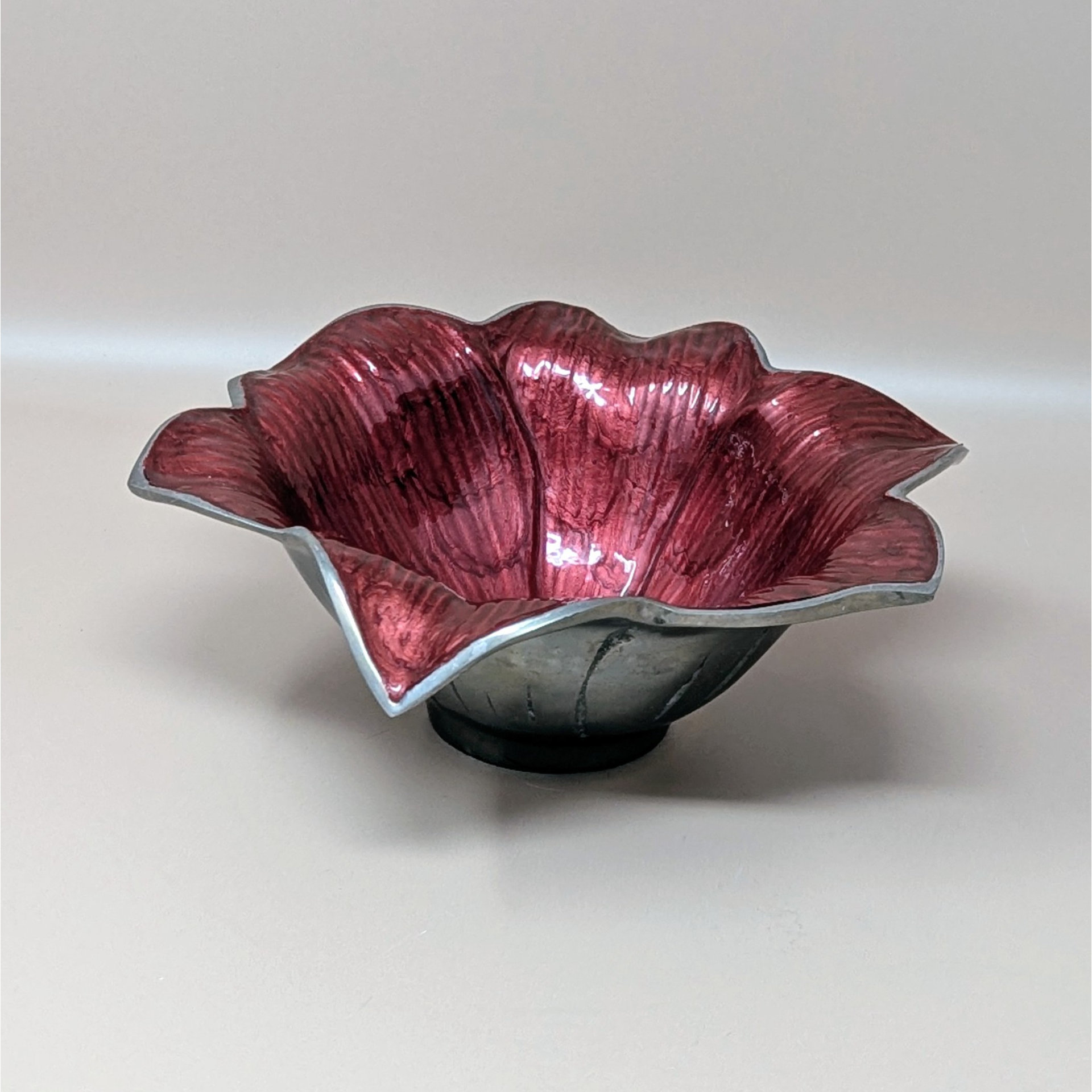 A floral-shaped bowl with a vibrant deep red enamel interior and a silver-toned aluminum exterior. The bowl features wavy, petal-like edges and a textured finish, shown against a neutral background.