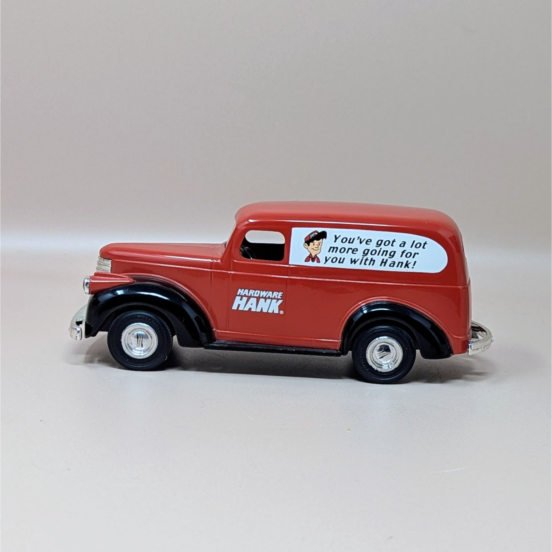 A red and black die cast metal 1946 Chevy Suburban van replica in its original box. The side of the van features the Hardware Hank logo and a cartoon mascot with a slogan.