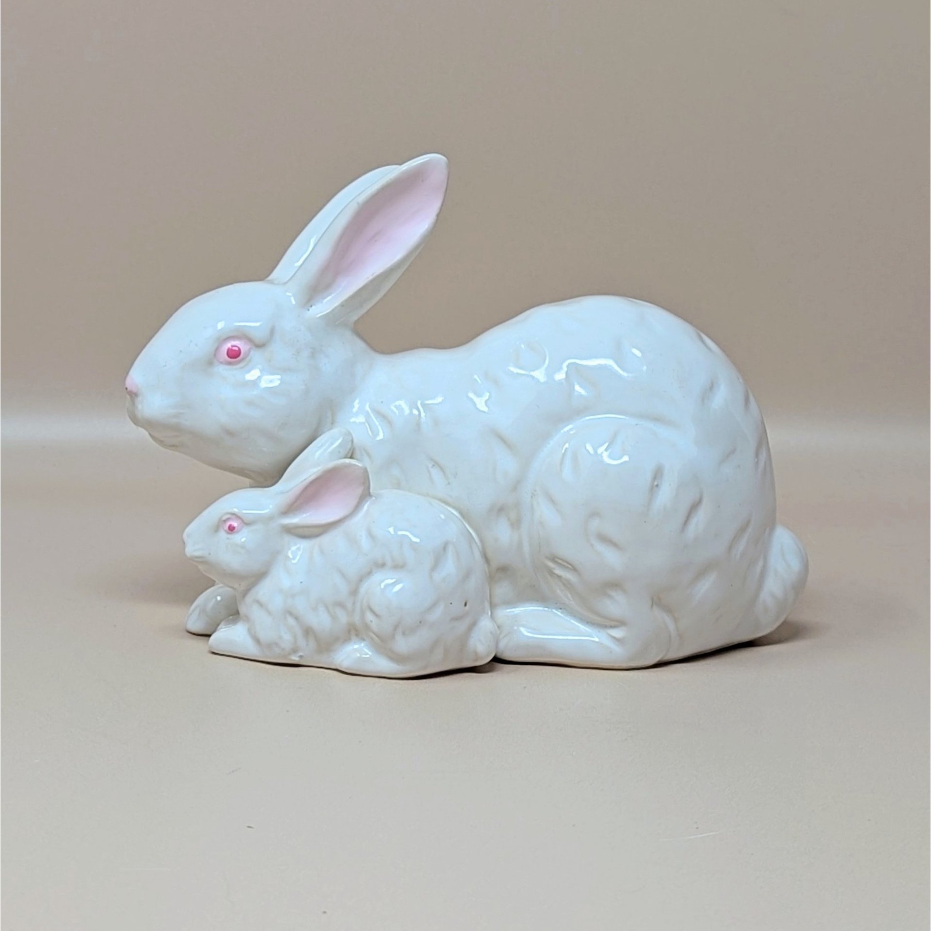 A vintage white ceramic figurine by Rosenthal Netter featuring a mother rabbit and her baby tucked beside her. The bunnies have pink eyes and ears with a subtle textured fur pattern in the glaze.