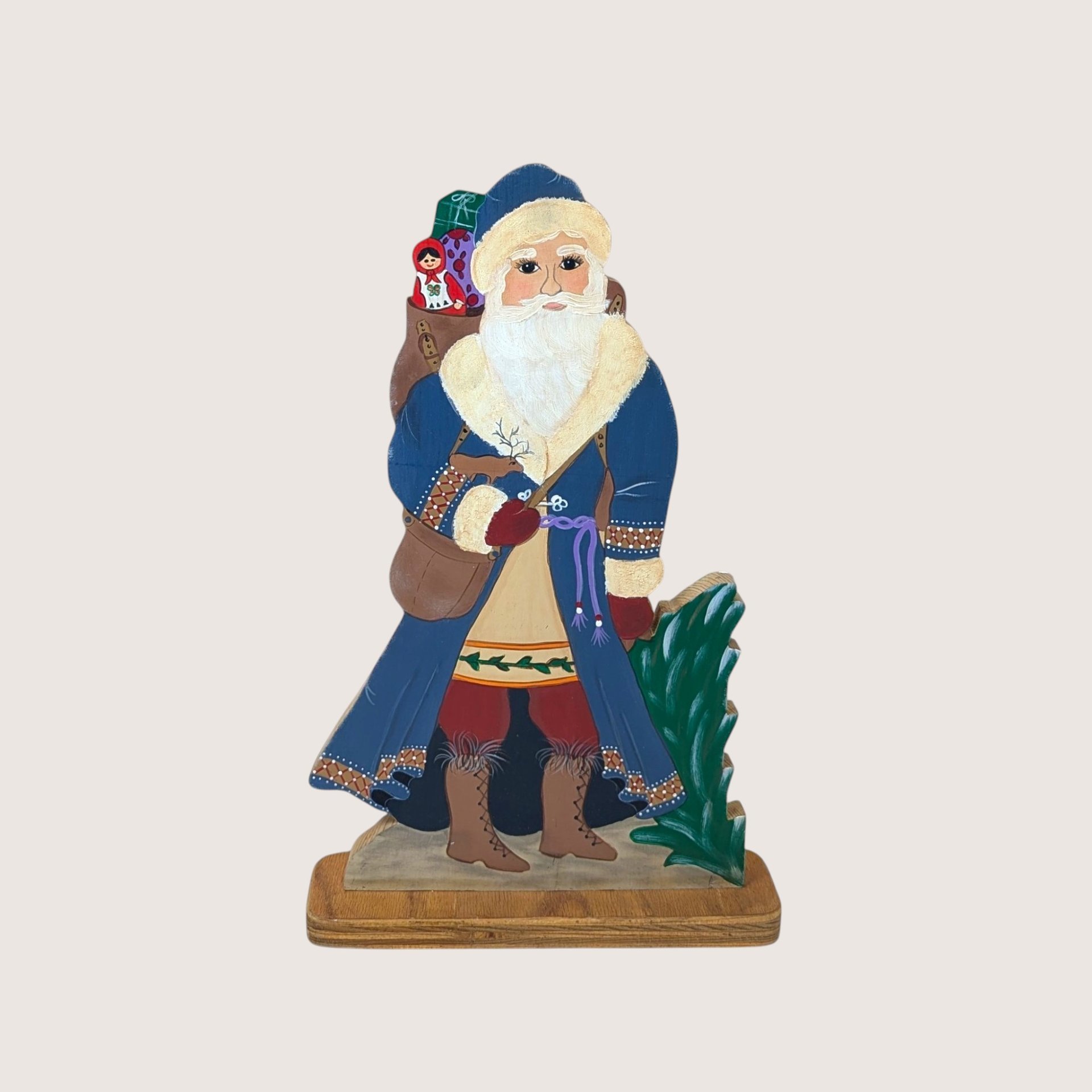 Hand painted wooden Santa Claus figure wearing a blue coat and holding a sack with a matryoshka doll.