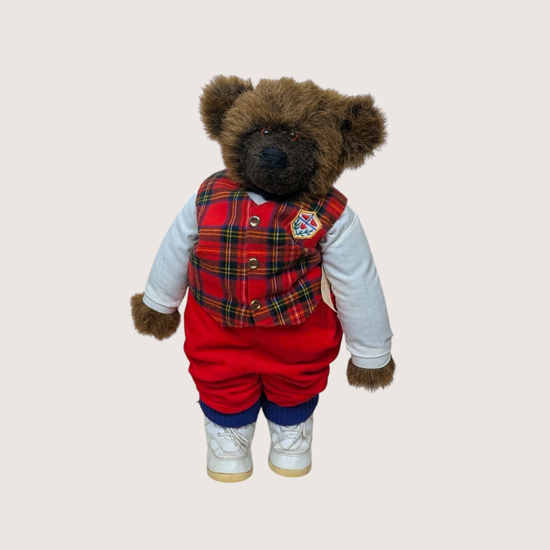 A jointed handmade artist teddy bear named Ted Edward wearing a plaid vest red trousers and white sneakers