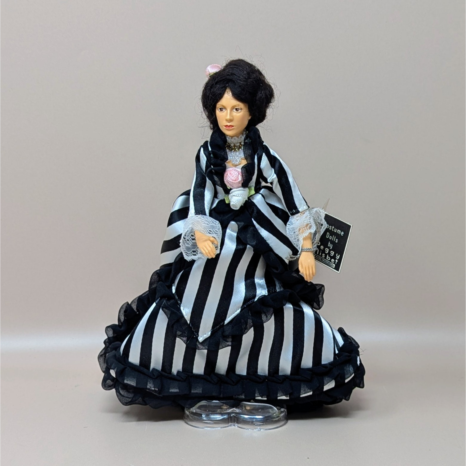 A vintage Peggy Nisbet portrait doll based on a Renoir painting. She wears a striking black and white striped gown with ruffled trim and lace cuffs. Her dark hair is styled up with a small pink rose.