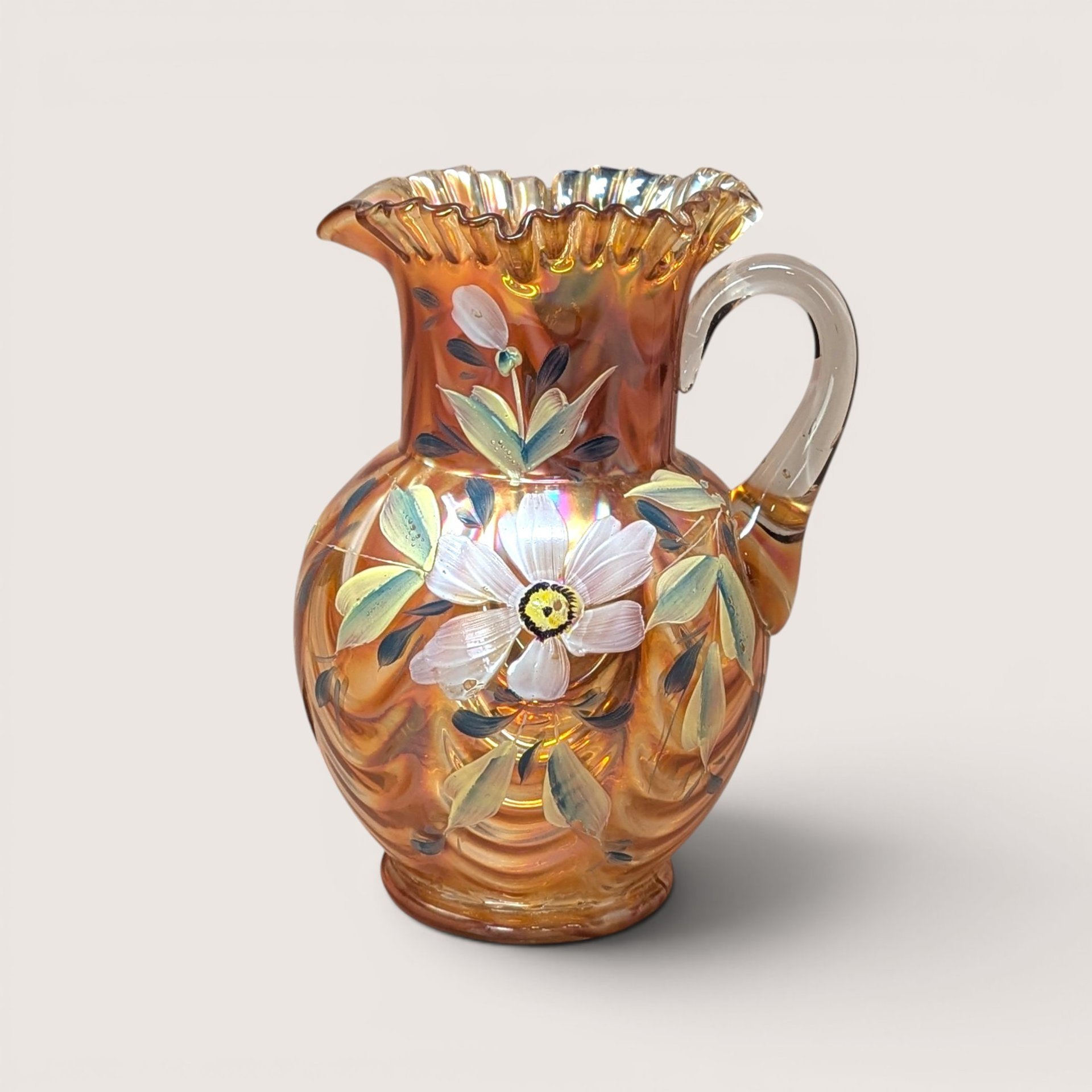 A handpainted marigold carnival glass pitcher with a ruffled rim and white floral details, centered on a beige background.