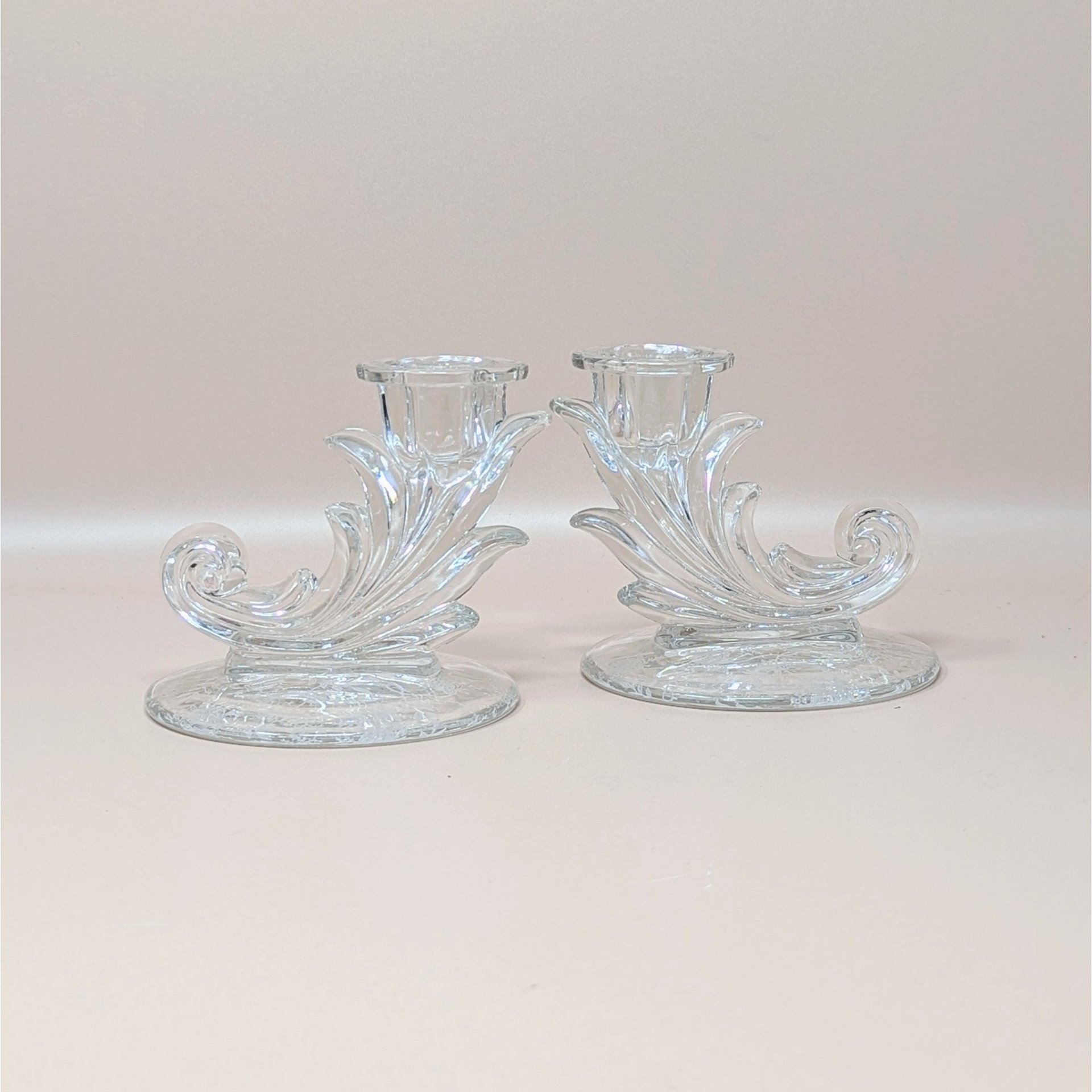 A pair of vintage clear glass cornucopia-shaped candlesticks by Fostoria in the Navarre pattern. The holders feature a decorative Baroque scroll design and an intricate etched floral pattern on the circular bases.