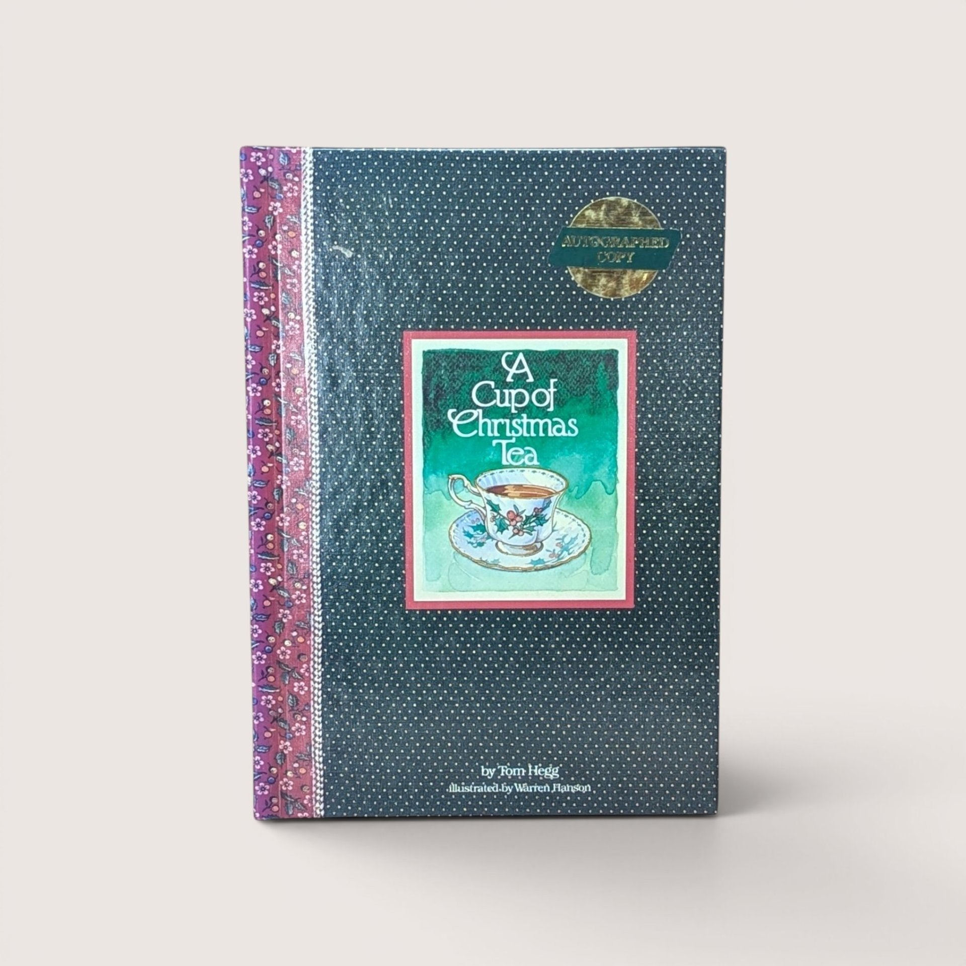 An autographed holiday book titled A Cup of Christmas Tea with a teacup illustration, centered on a beige background.