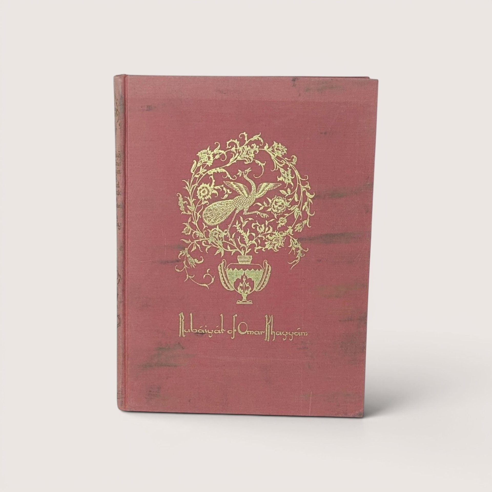 A vintage rose pink cloth hardcover book featuring a gold gilt peacock medallion on the front cover