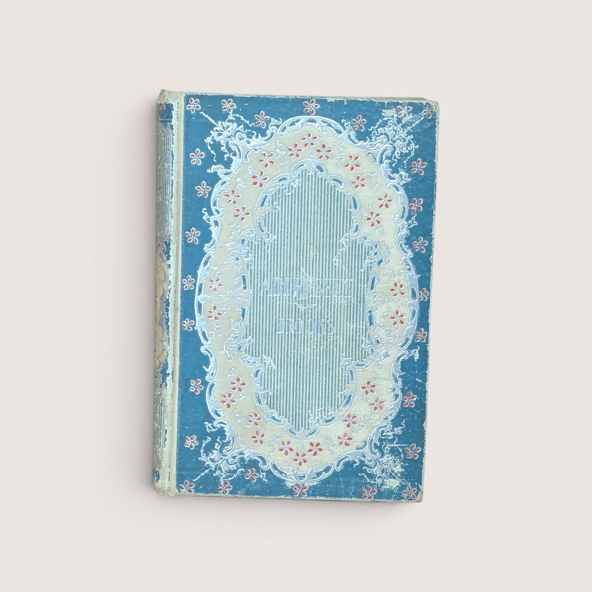 An antique blue and cream hardcover book featuring an ornate floral filigree border on the front cover