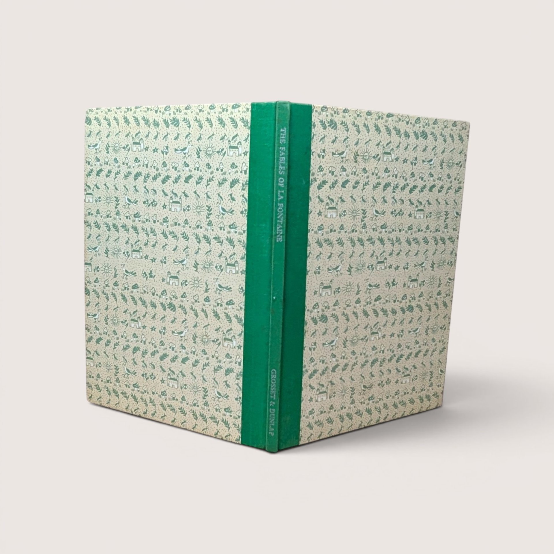 A vintage hardcover book standing upright showing a green cloth spine and patterned cream and green boards