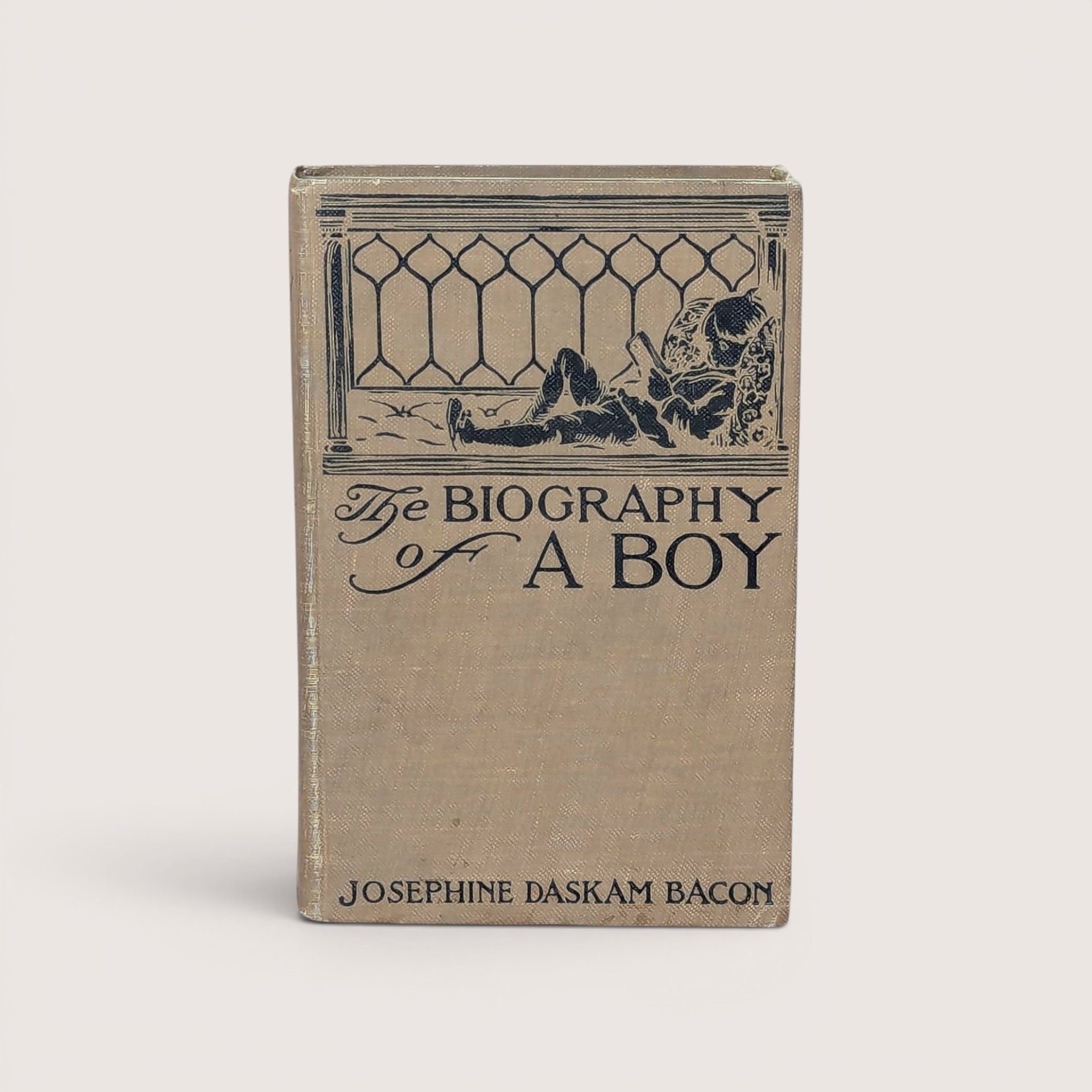 An antique beige cloth hardcover book with a dark green illustration of a boy lounging and reading