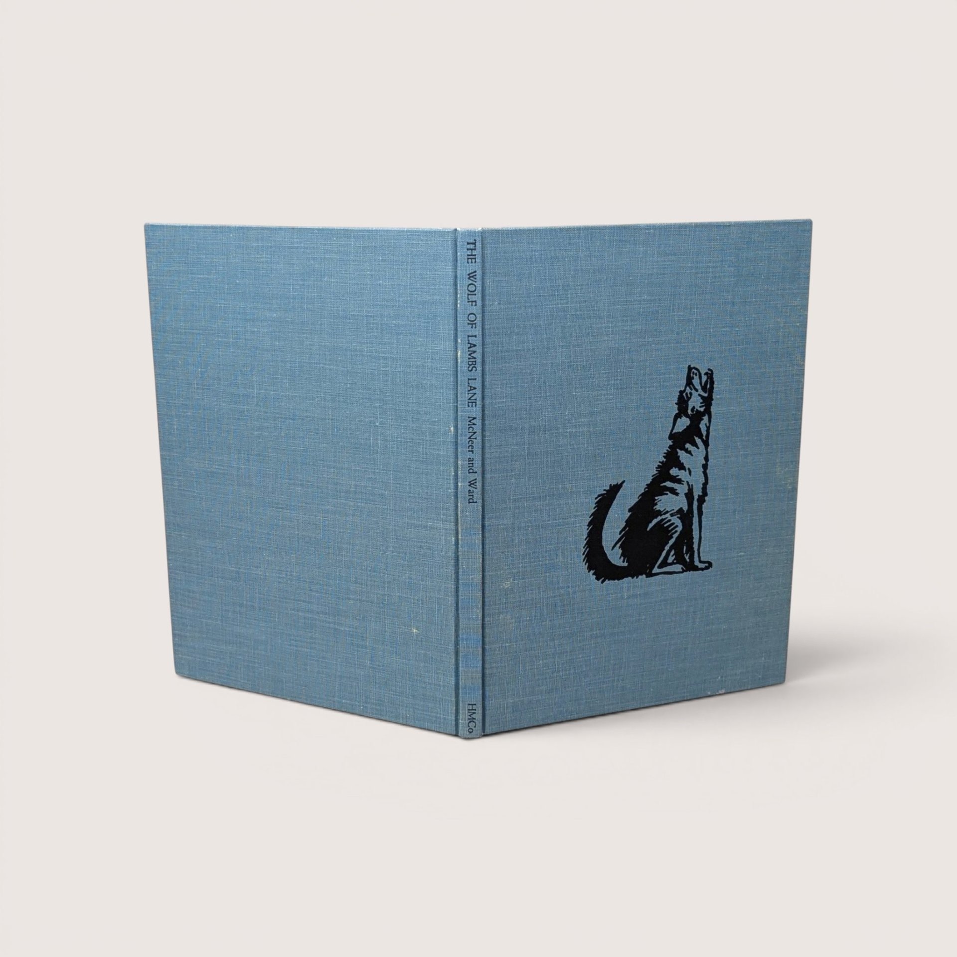 A vintage blue cloth hardcover book standing upright showing a black stamped illustration of a howling wolf on the front cover