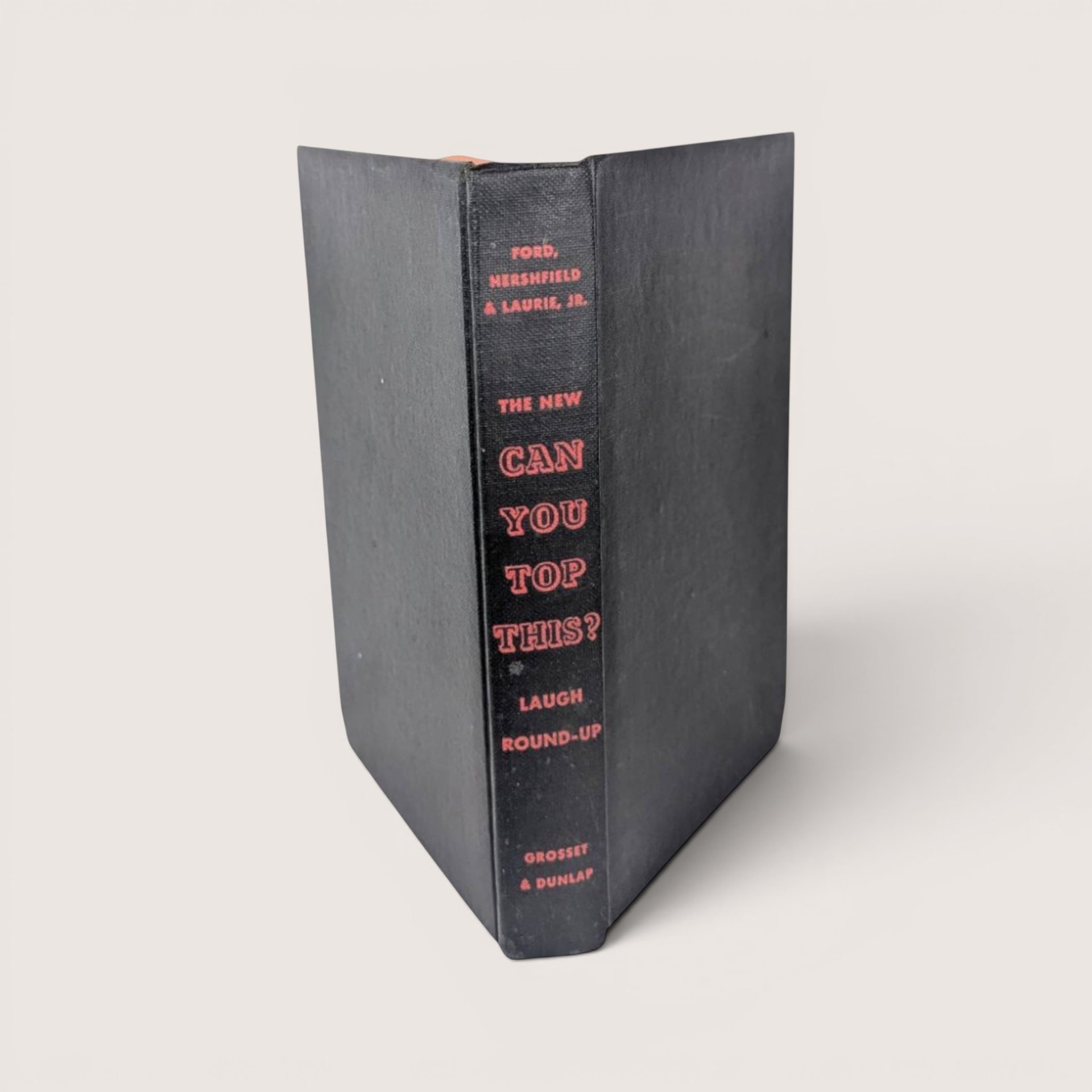 Vintage hardcover book spine in textured black cloth with bright red embossed text reading The New Can You Top This.