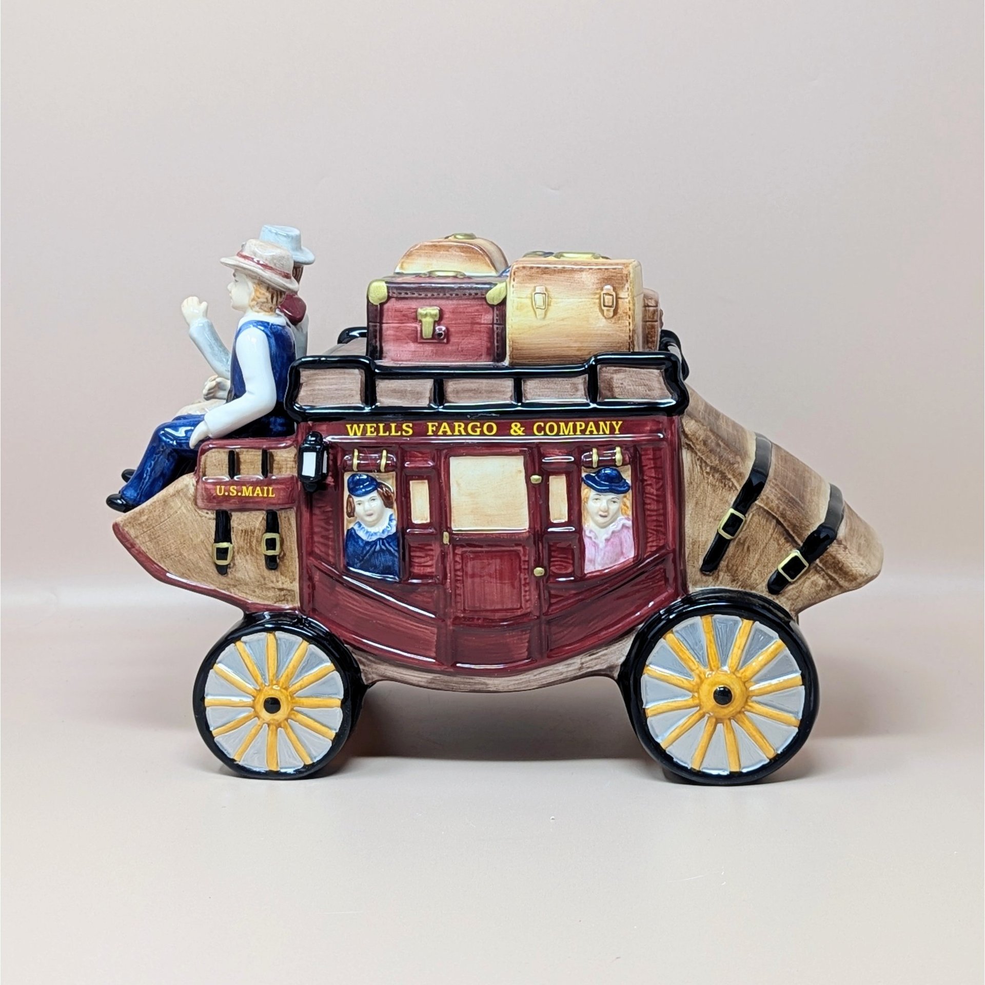 A large vintage ceramic cookie jar shaped like a Wells Fargo & Company stagecoach. The red and brown coach features hand-painted passengers, rooftop luggage, and yellow-spoked wheels.