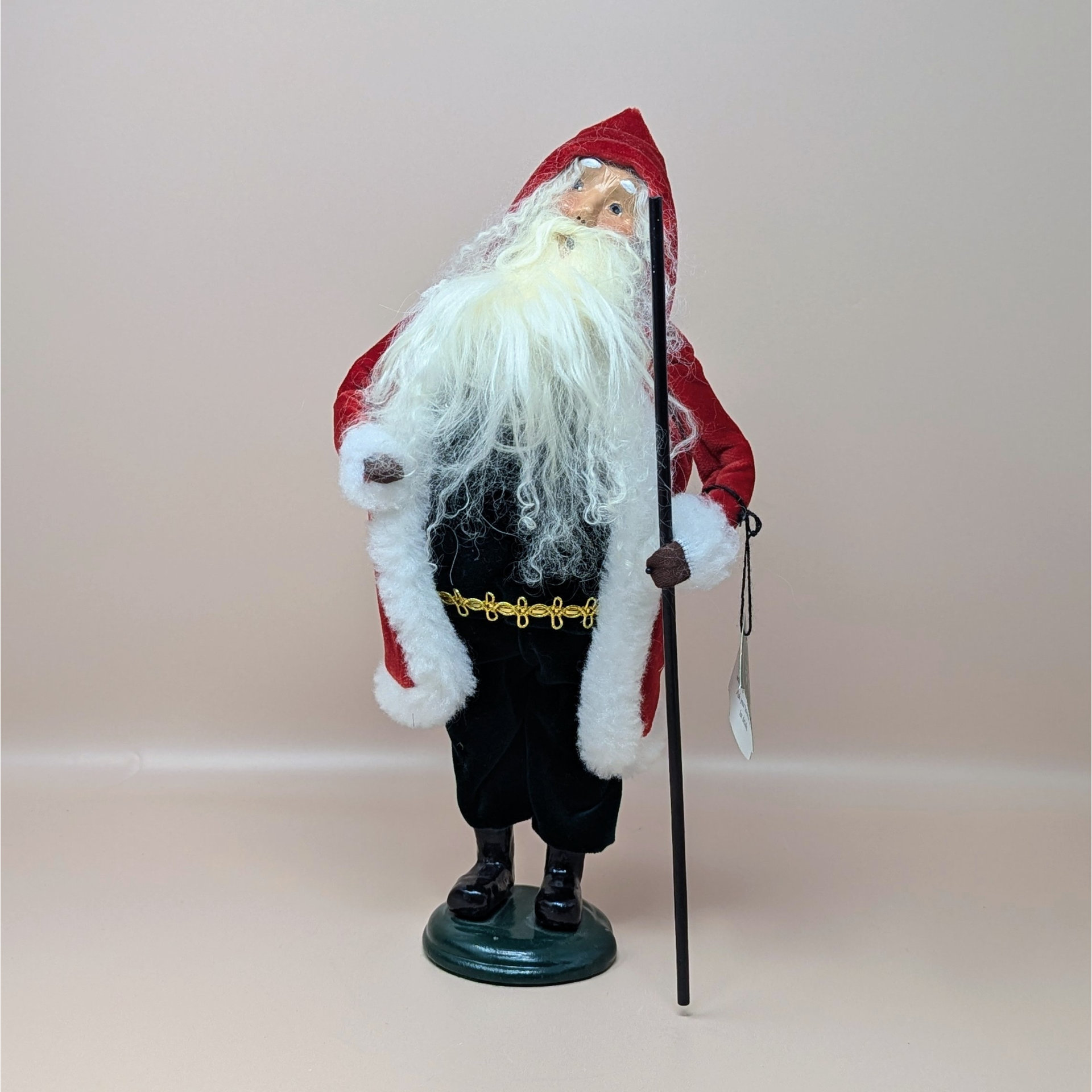 A 1999 Byers Choice Caroler figure depicting a Victorian-style Santa Claus. He is wearing a deep red velvet hooded coat with white faux fur trim, black pants, and carrying a tall black staff.