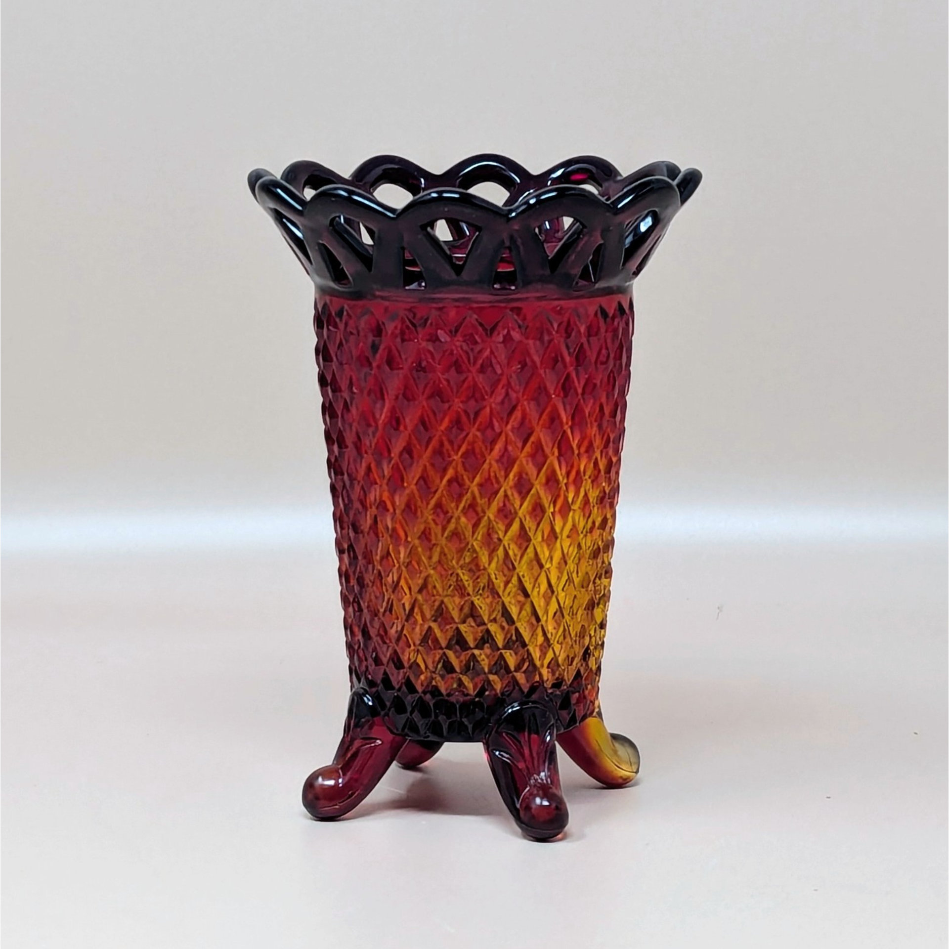 A vintage Imperial Glass Amberina vase (C3319 1.jpg) with a diamond point texture and a lace-cut reticulated rim. The glass transitions from ruby red at the top to golden amber at the base, standing on three small feet.
